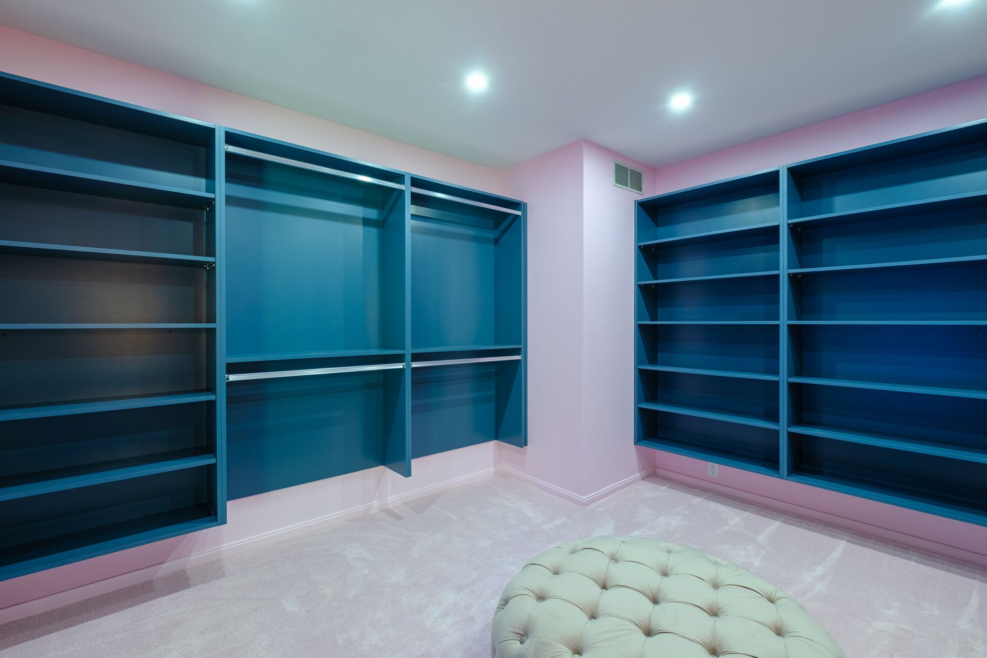 Walk-in closet with teal shelving and racks, pink walls and floor, and an ottoman.