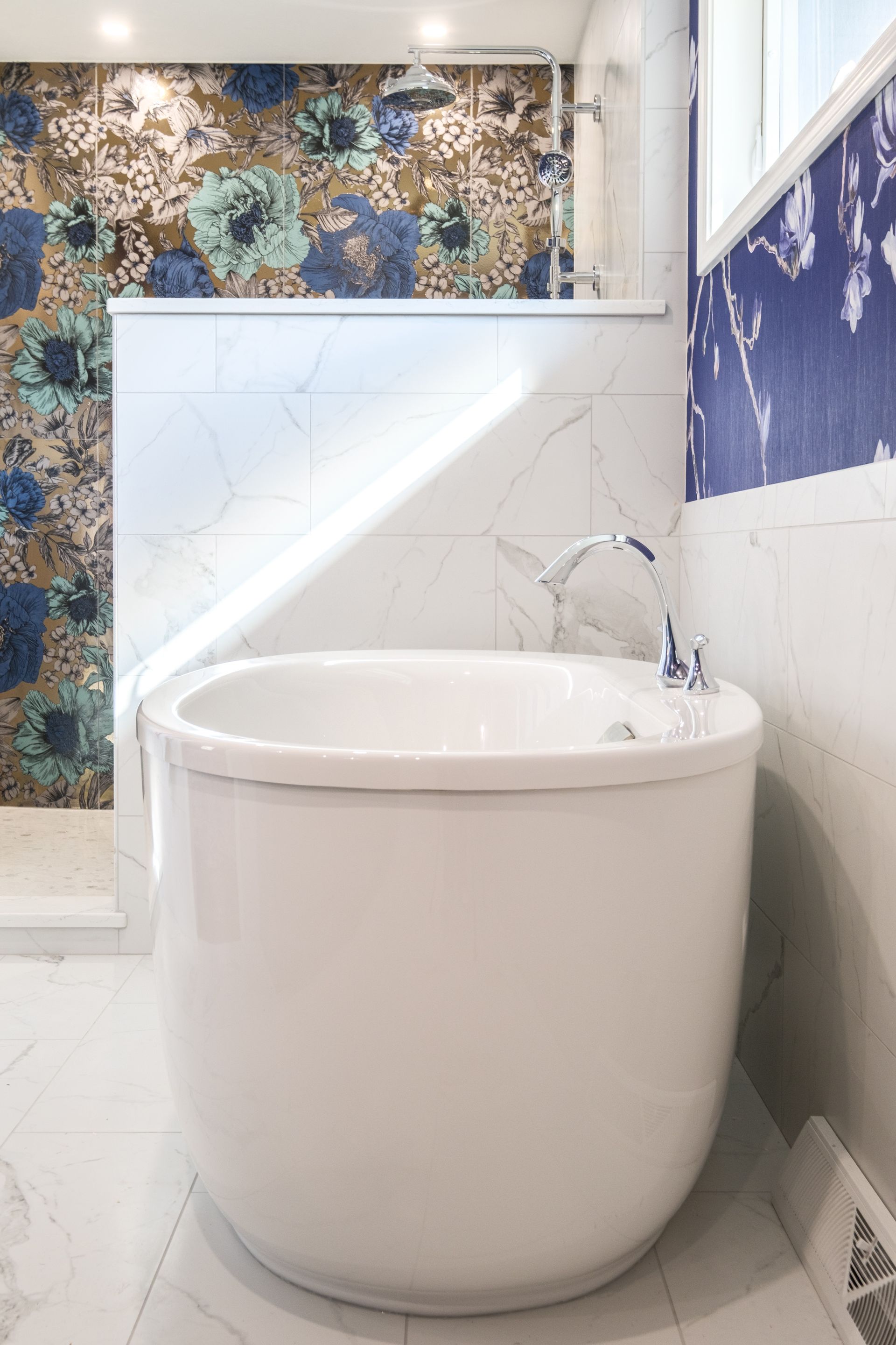 White oval bathtub in a modern bathroom with floral patterned accent tile and marble walls.