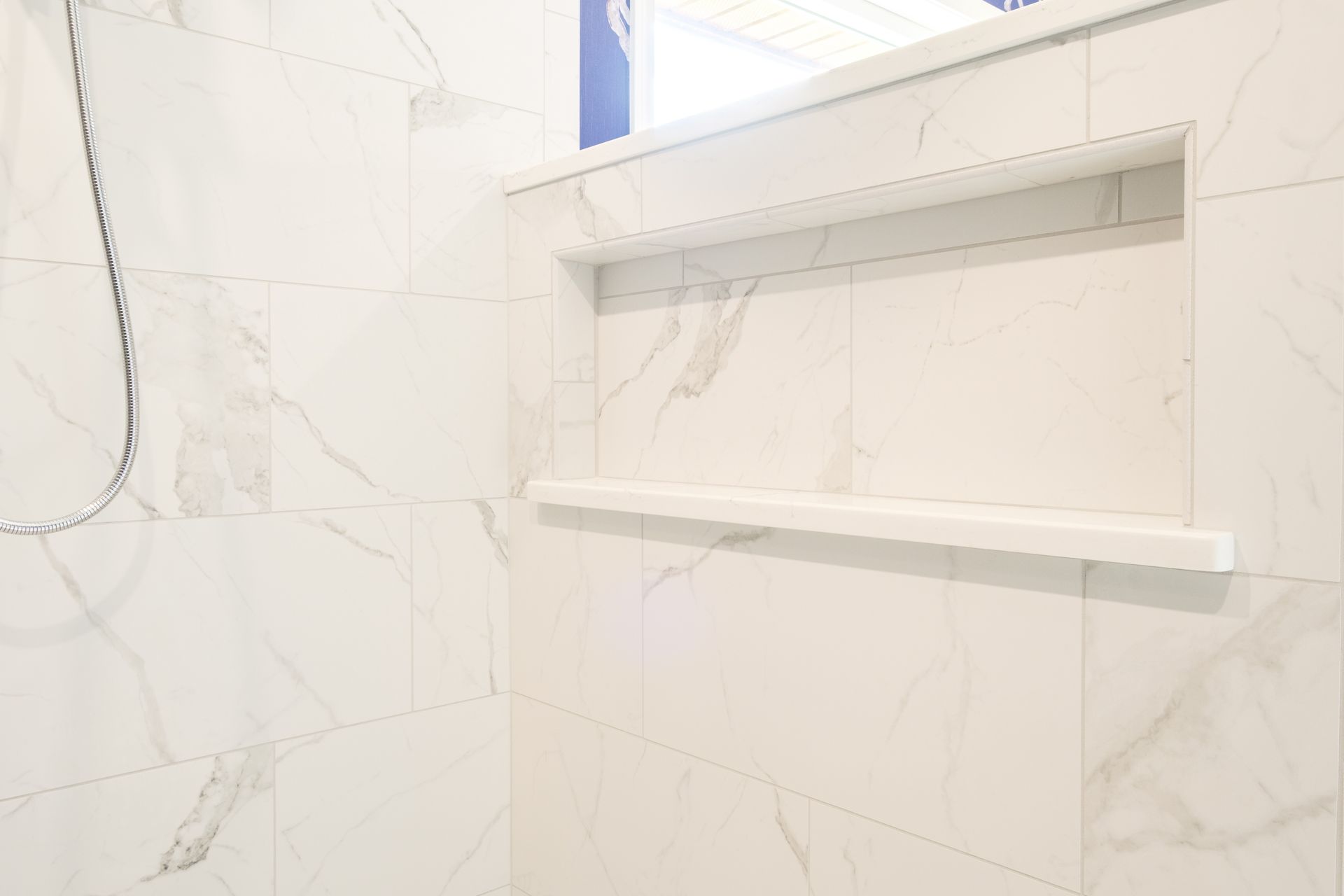 White marble shower with built-in shelf.