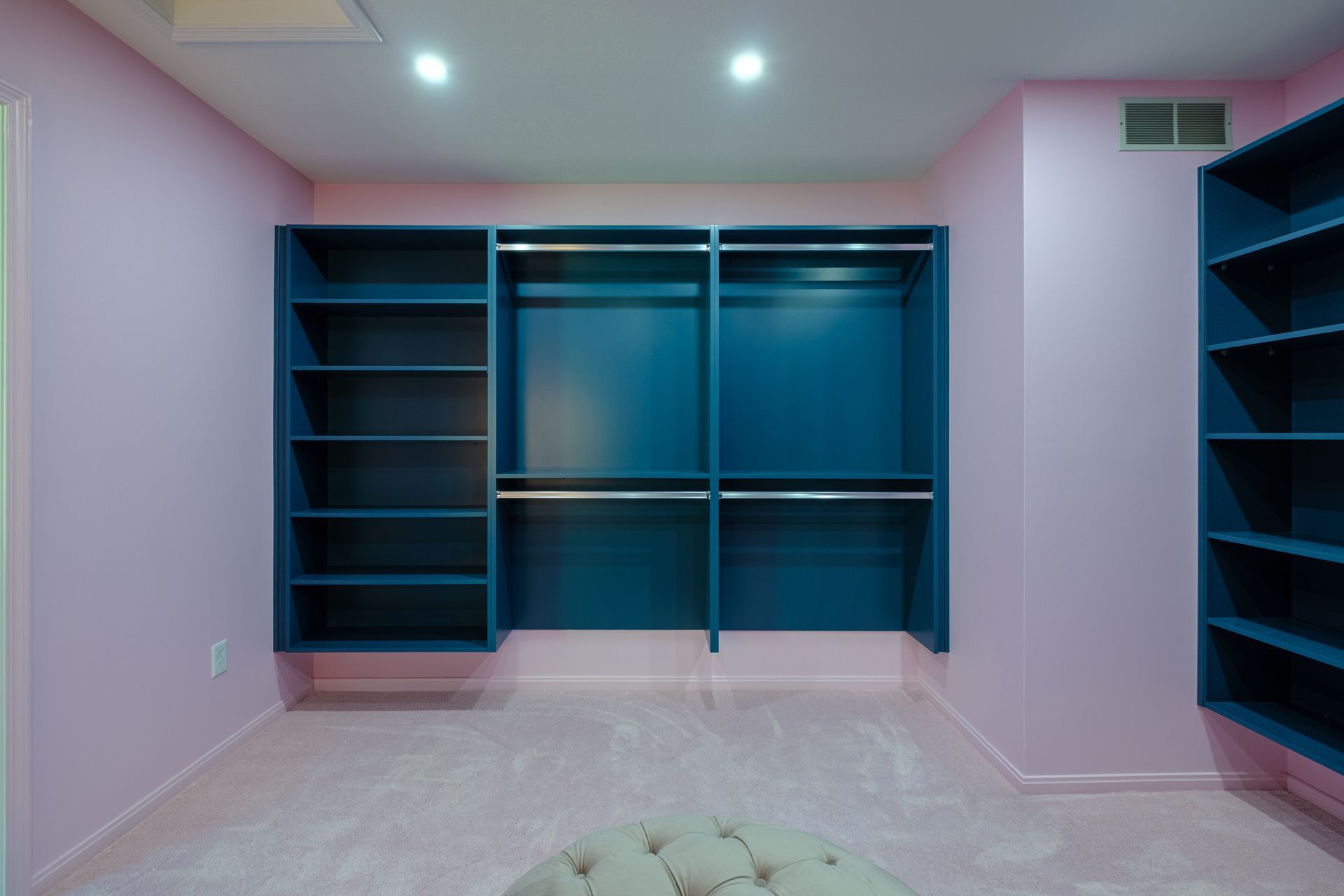 Empty walk-in closet with teal shelving and rods against pink walls and a pink carpet.