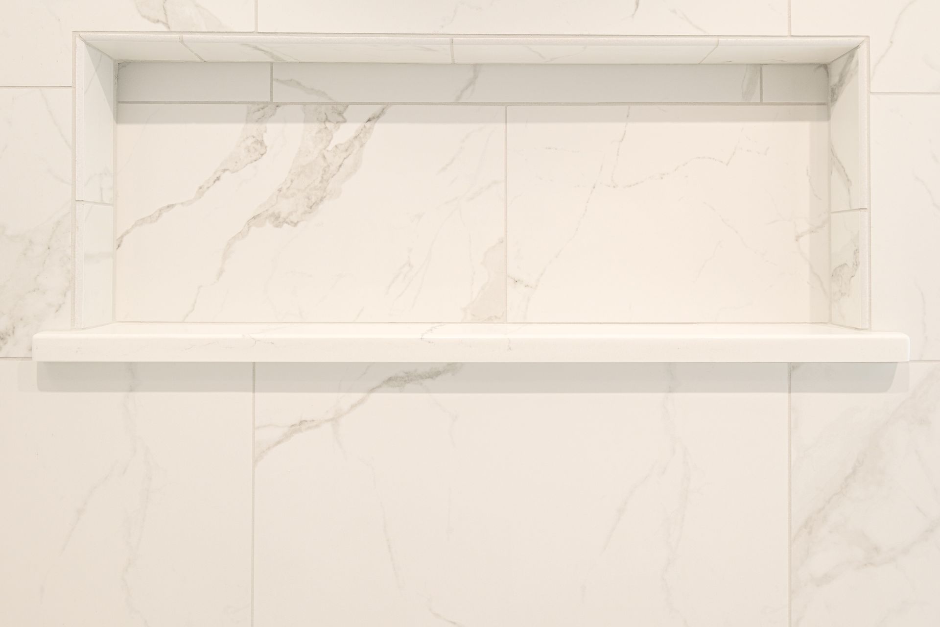 Rectangular recessed shelf in a white marble tiled shower.