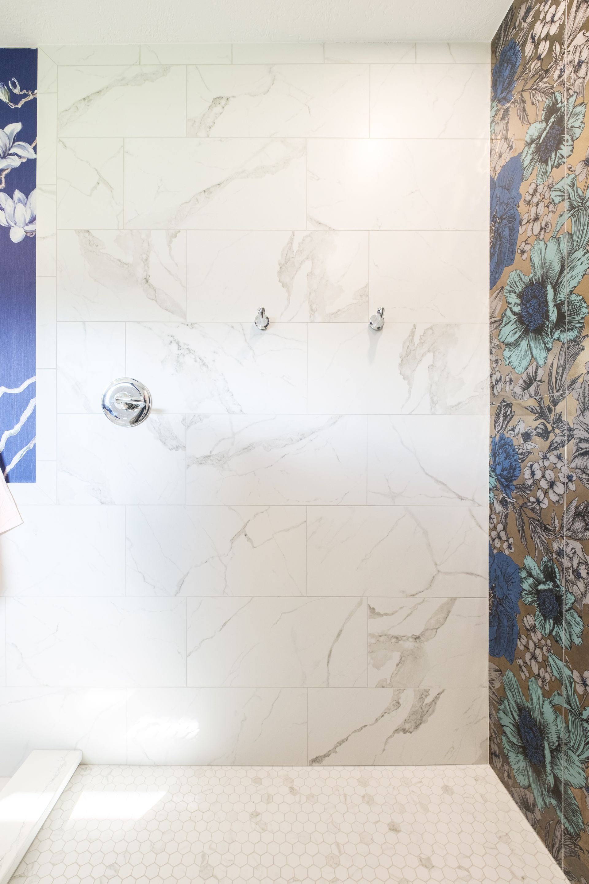 Shower with white marble walls, floral accent wall, and patterned floor.