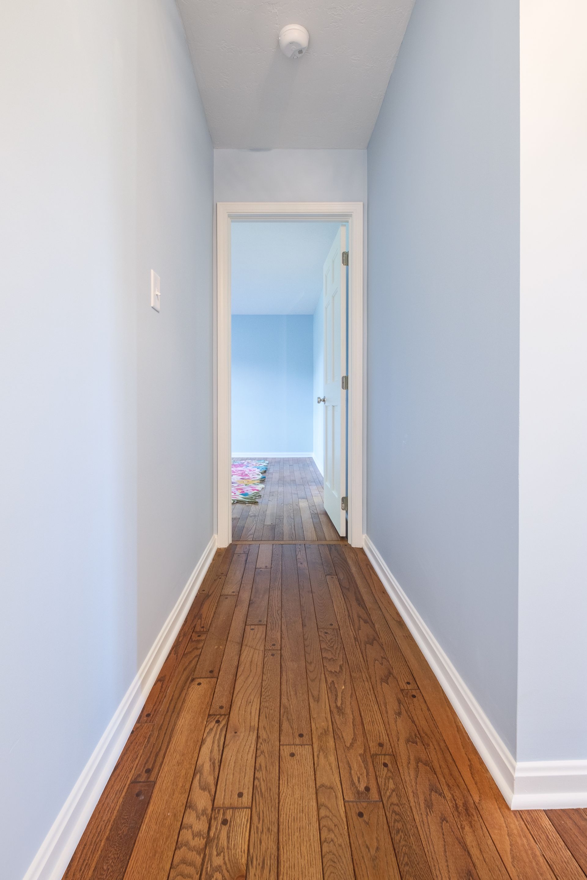 Long hallway with wood floor, pale blue walls, and doorway at end.