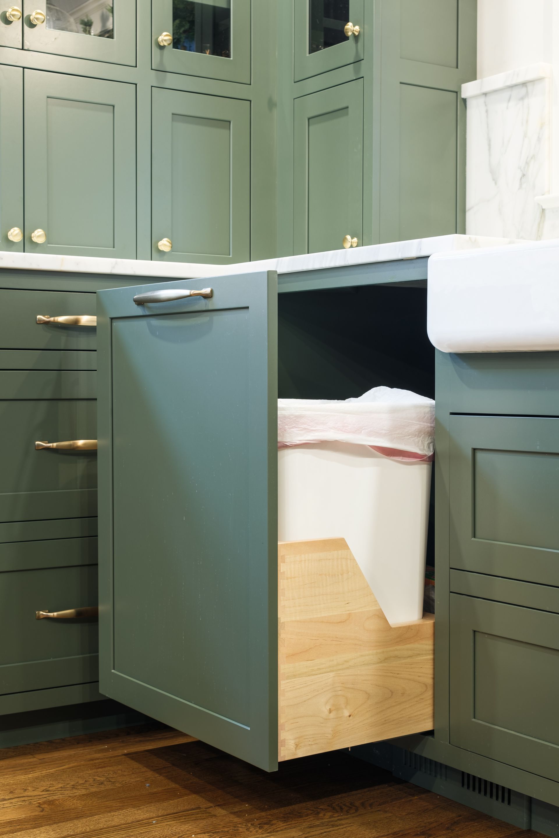 A trash can is pulled out of a cabinet in a kitchen.