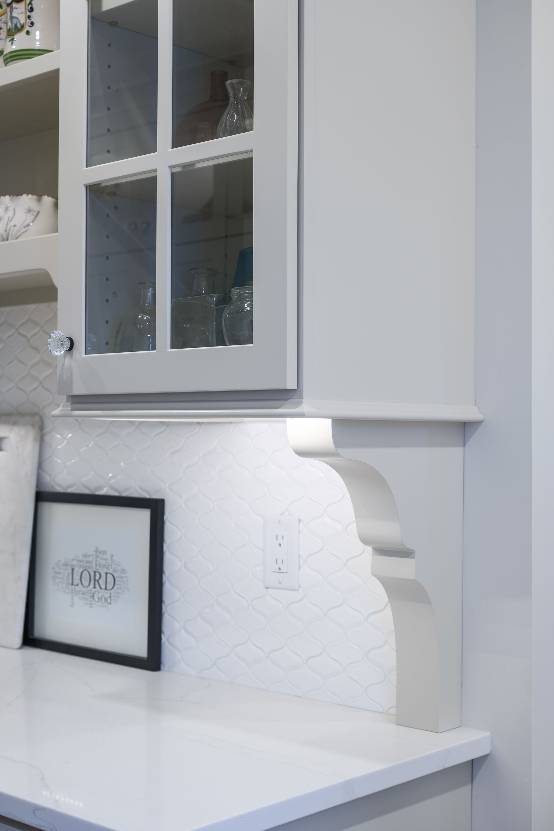 White kitchen counter with gray cabinets and decorative trim; picture frame and electrical outlet visible.