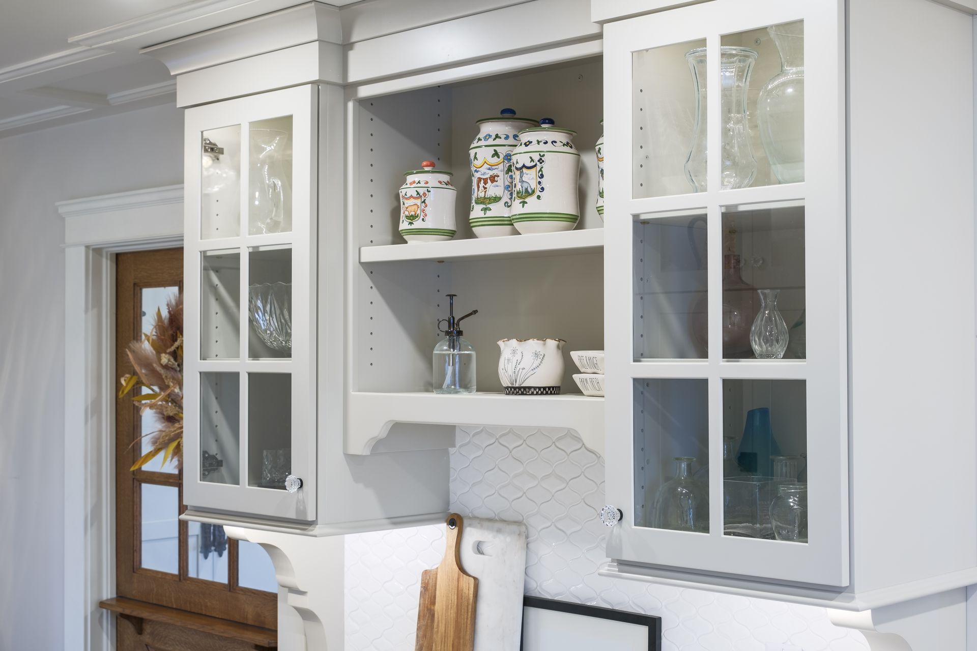 A kitchen with white cabinets and glass doors filled with pots and pans.