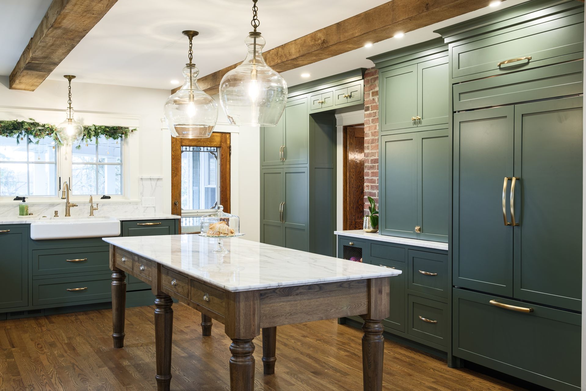Green kitchen with marble island, wooden beams, and glass pendant lights.