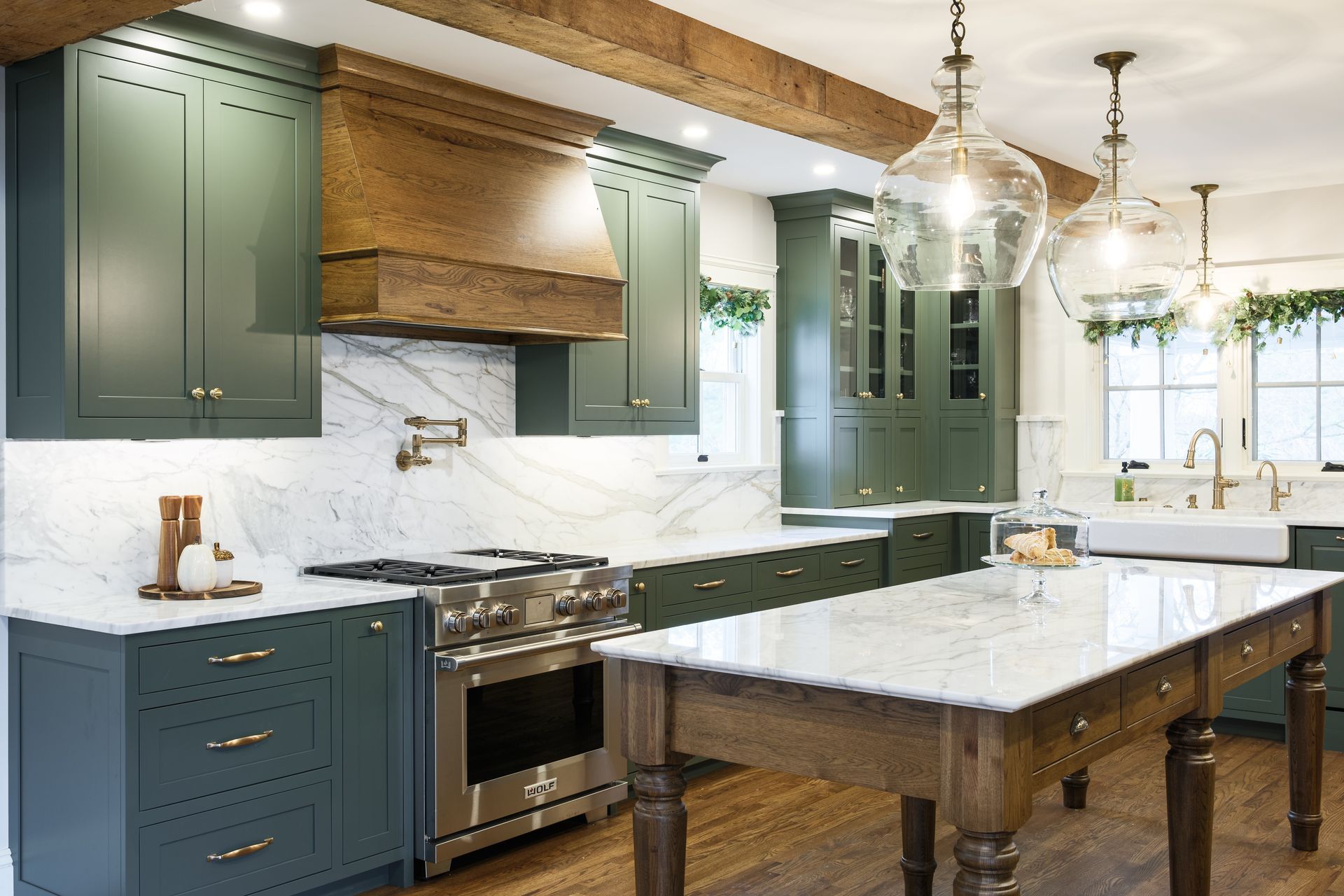Green kitchen with marble countertops, wood accents, and large glass pendant lights.