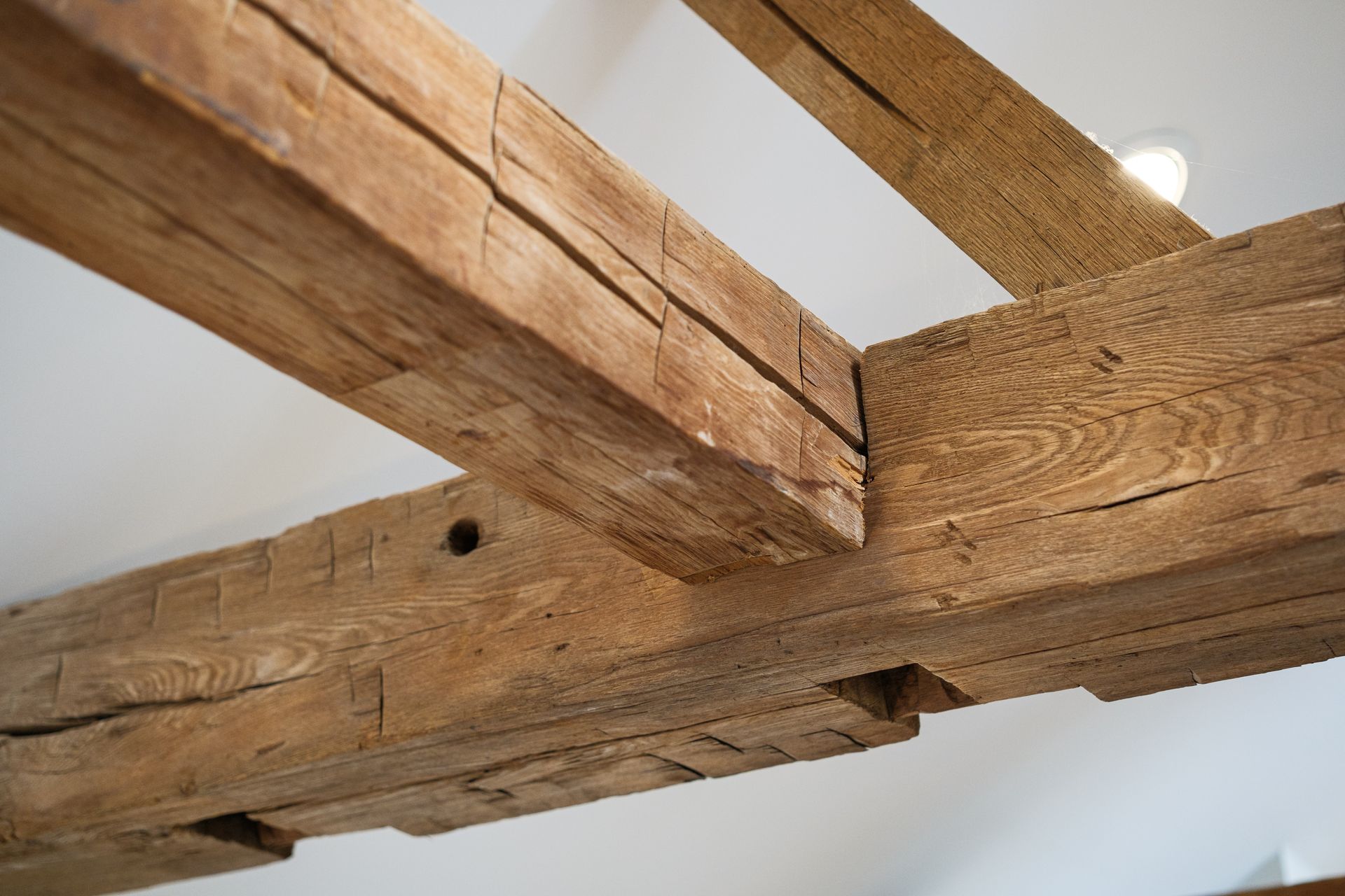 Wooden ceiling beams, weathered and textured, intersect against a white ceiling.