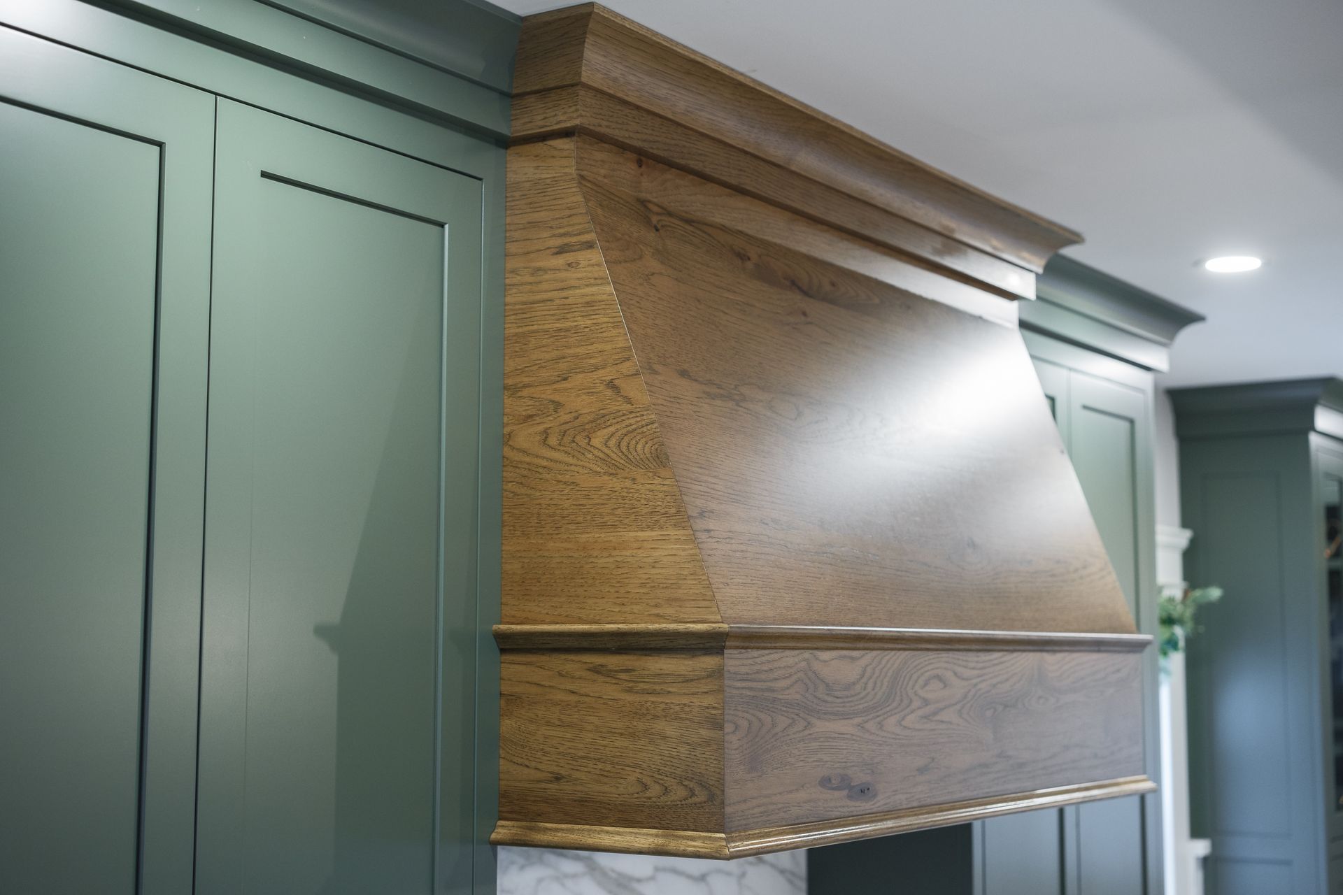 Green kitchen cabinets with a wooden range hood.