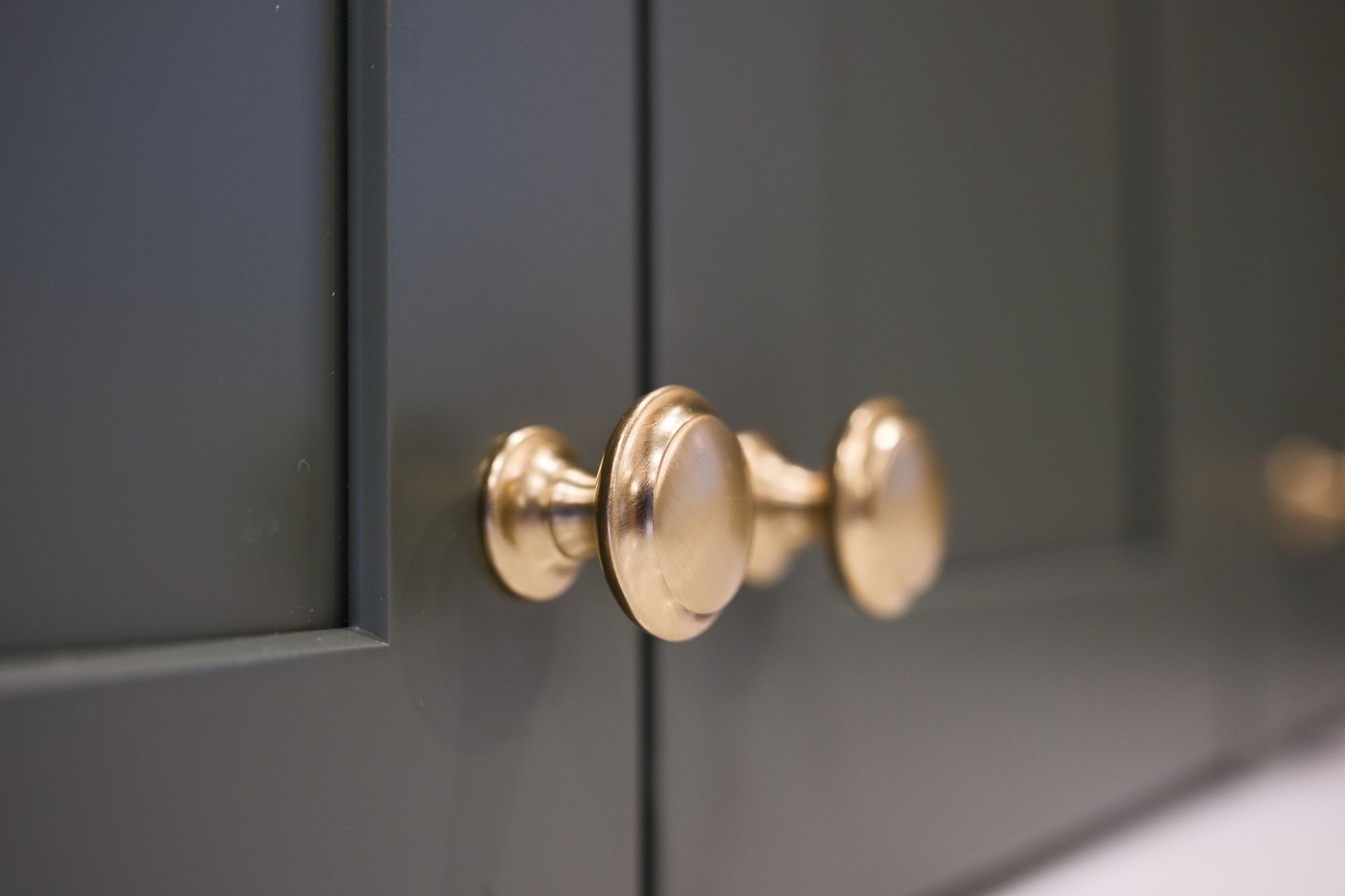 Brass cabinet knobs on a dark green cabinet, close-up.
