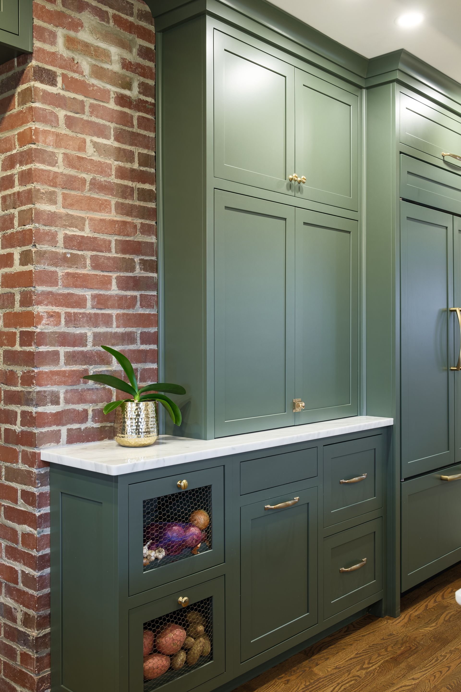 A kitchen with green cabinets and a brick wall.