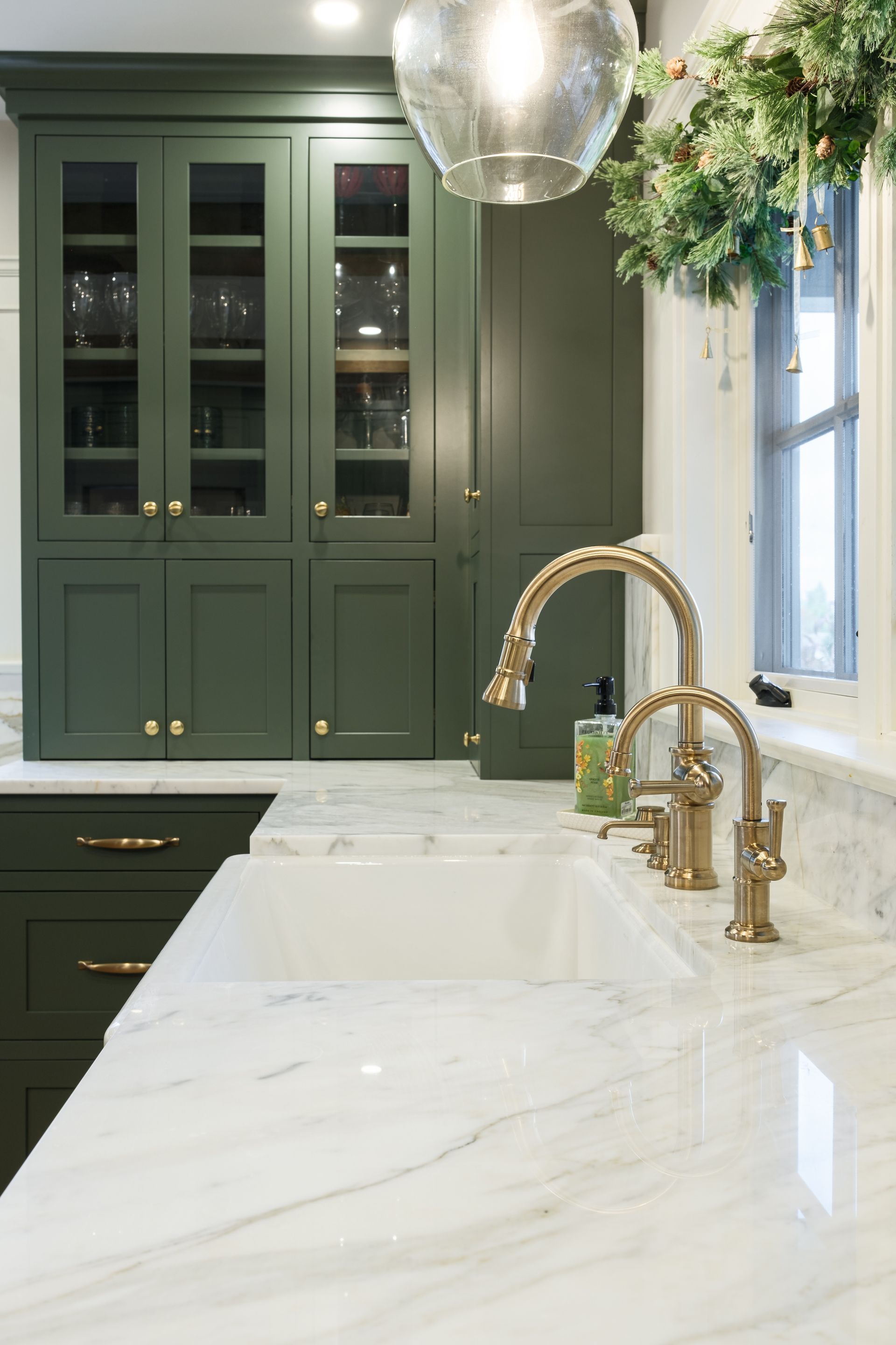 A kitchen with green cabinets , white counter tops , and a sink.