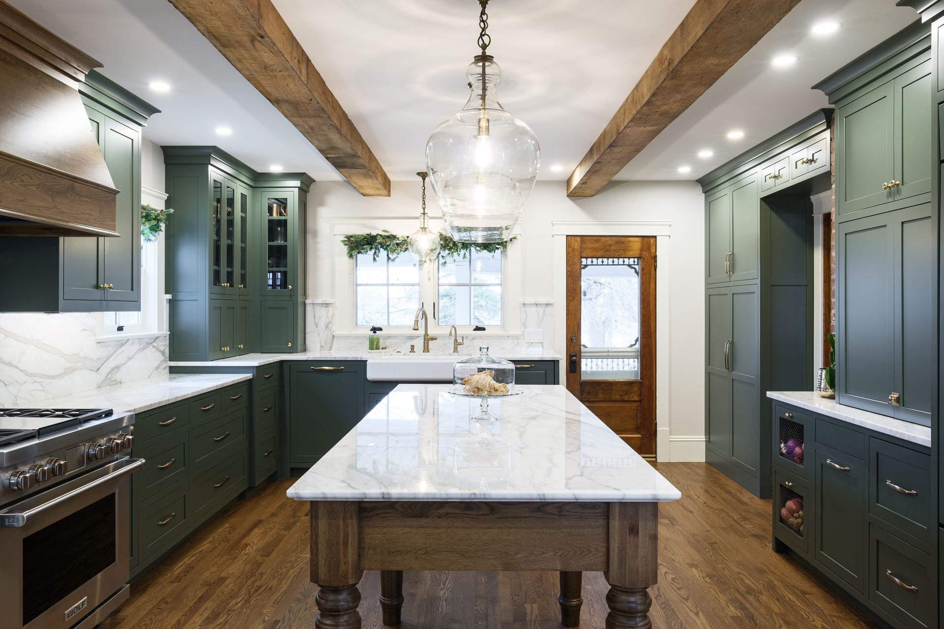 Green kitchen with marble countertops and a wooden island.