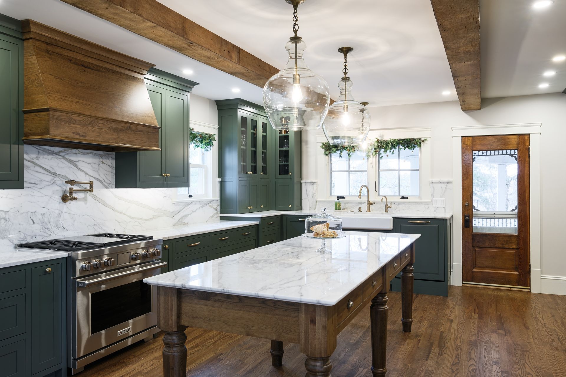 Green kitchen with marble countertops, wood beams, and a wooden island.