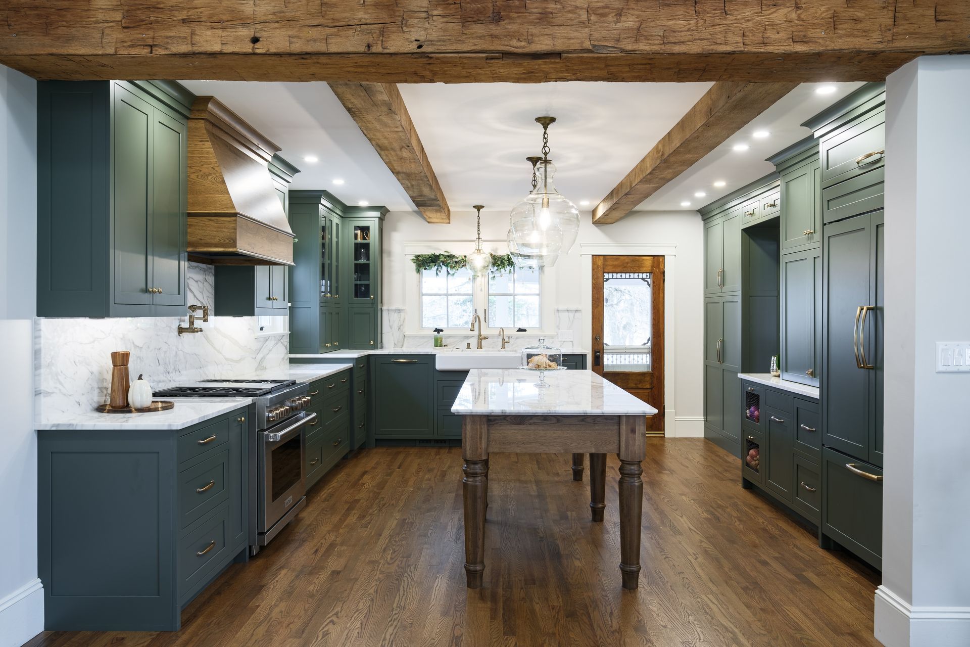 A kitchen with green cabinets , white counter tops , and a wooden table.