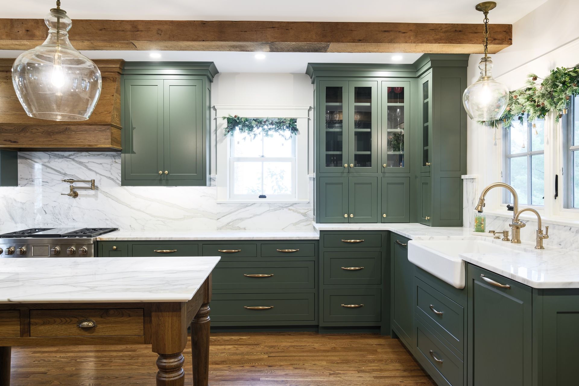 Green kitchen with marble countertops, wood accents, and decorative glass pendant lights.