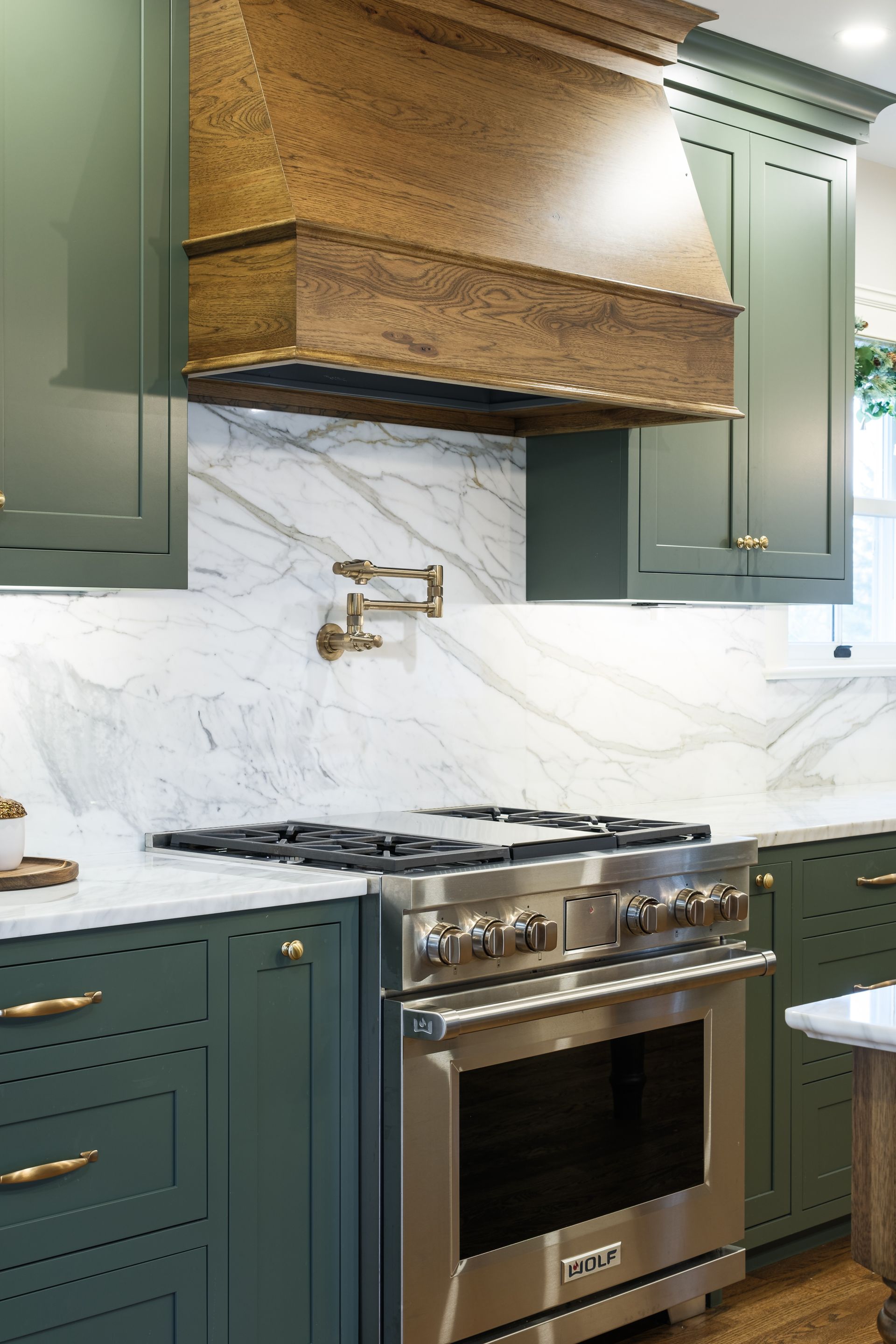 Green kitchen with stainless steel stove, marble backsplash, and brass fixtures.