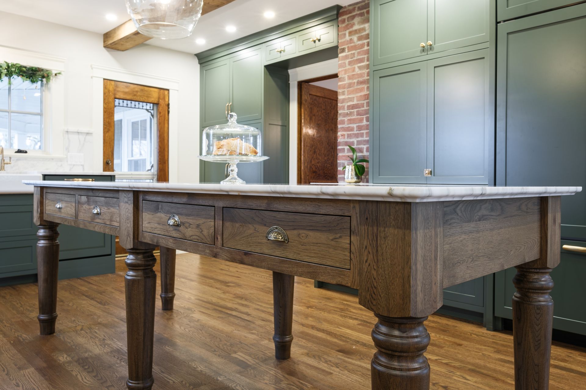 Kitchen with a wooden island, green cabinets, marble countertop, and wood flooring.