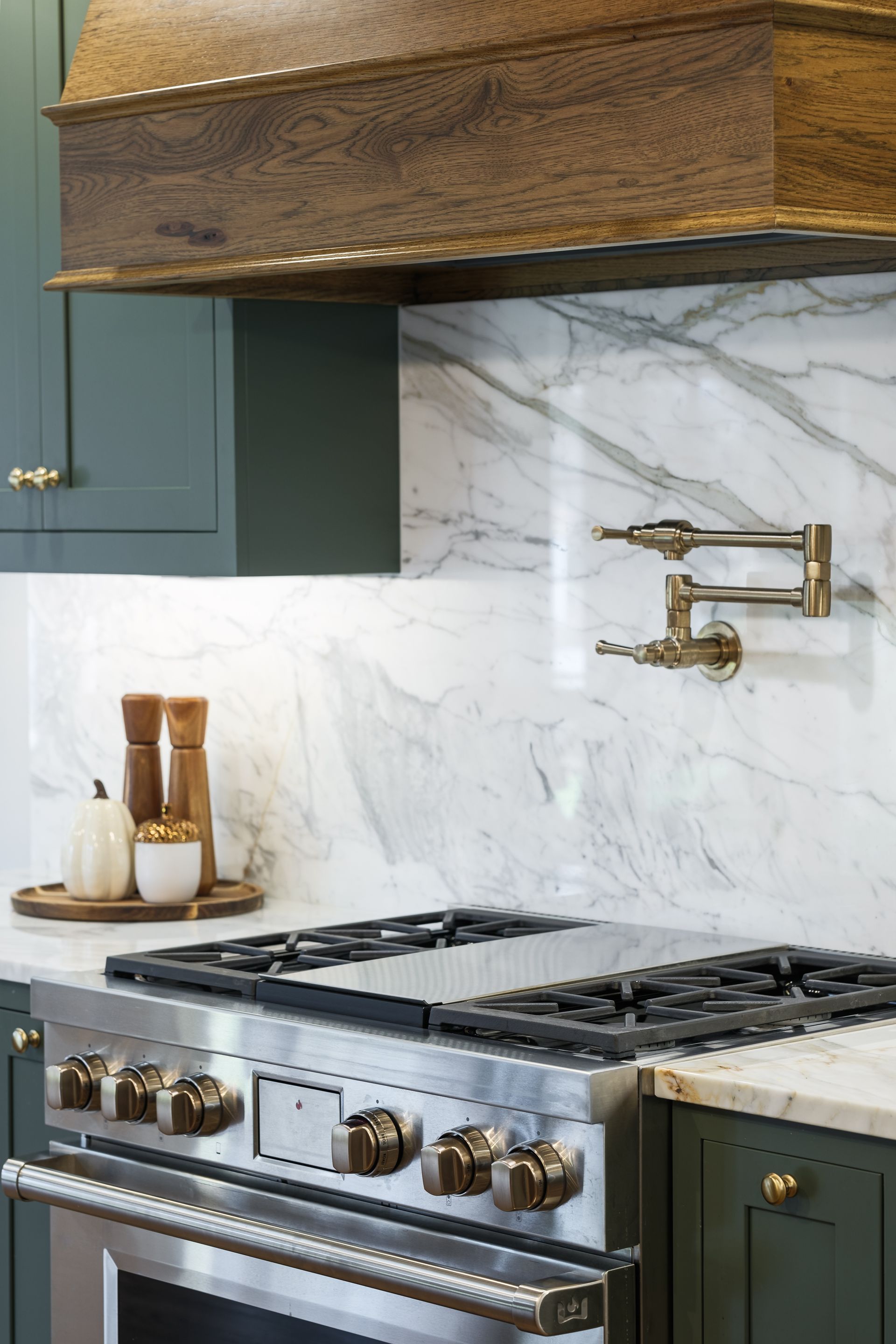 Green kitchen with marble backsplash, stainless steel range, and brass faucet.