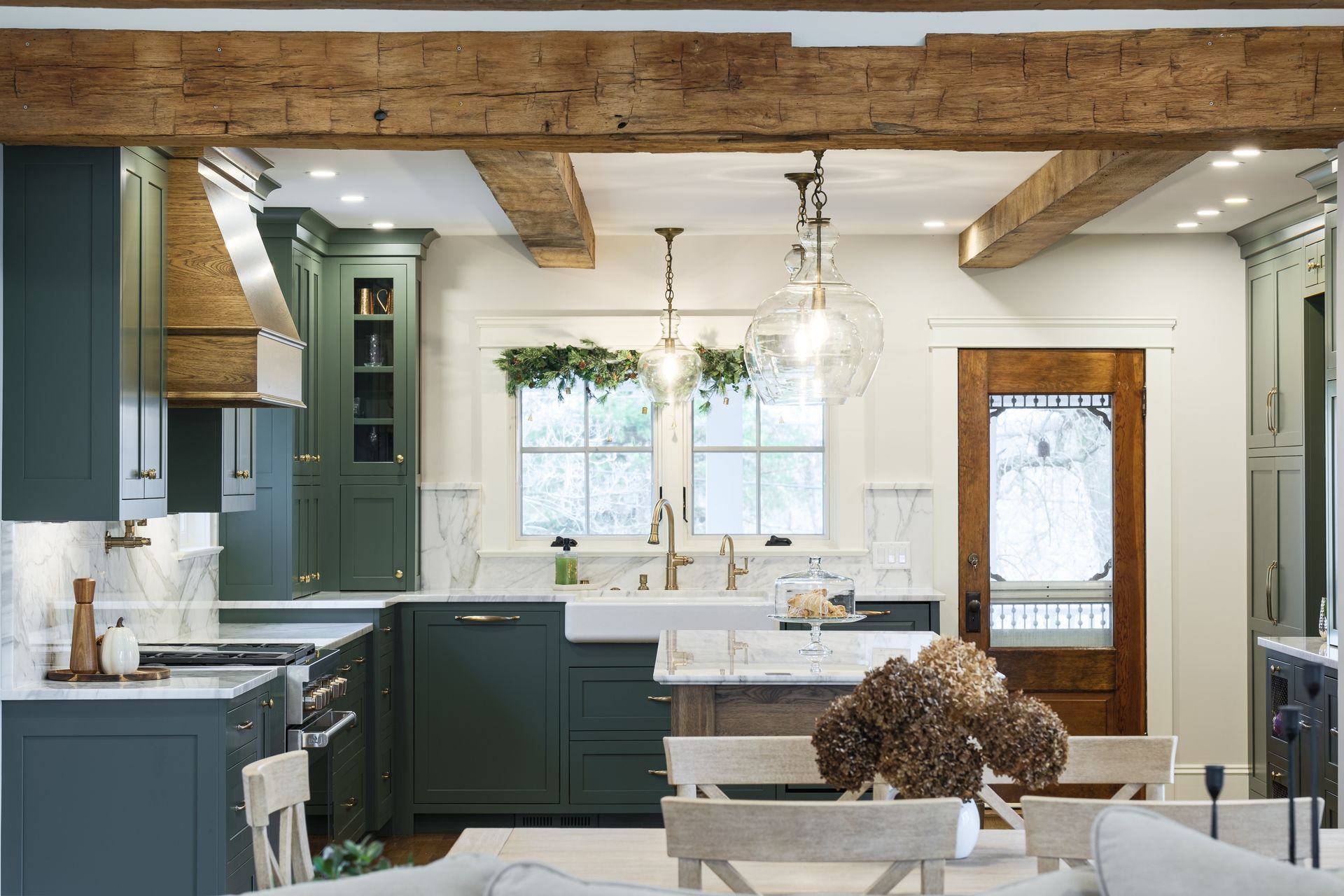 Green kitchen with wood beams, white countertops, a rustic door, and dining table.