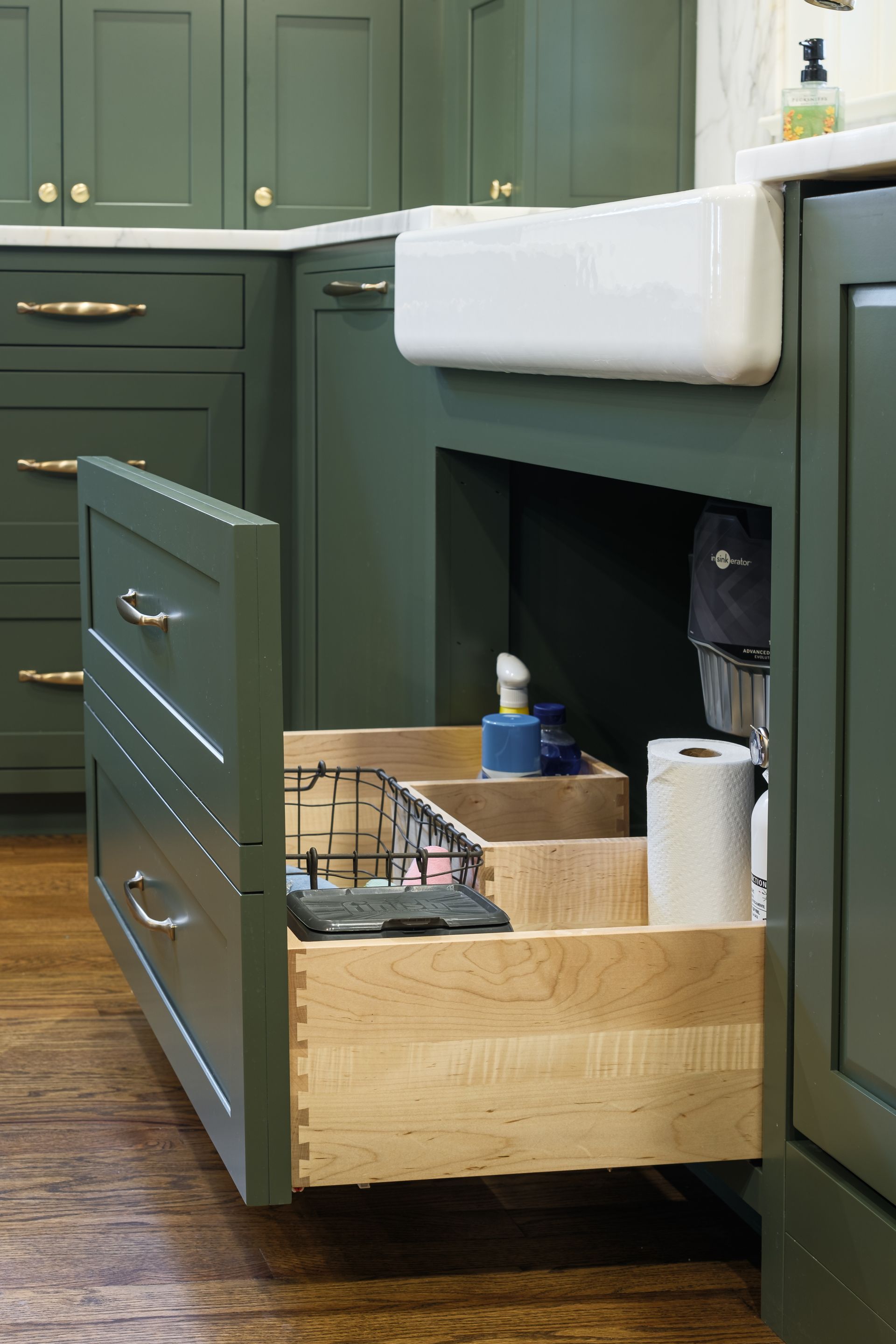 A kitchen with green cabinets and a wooden drawer under the sink.