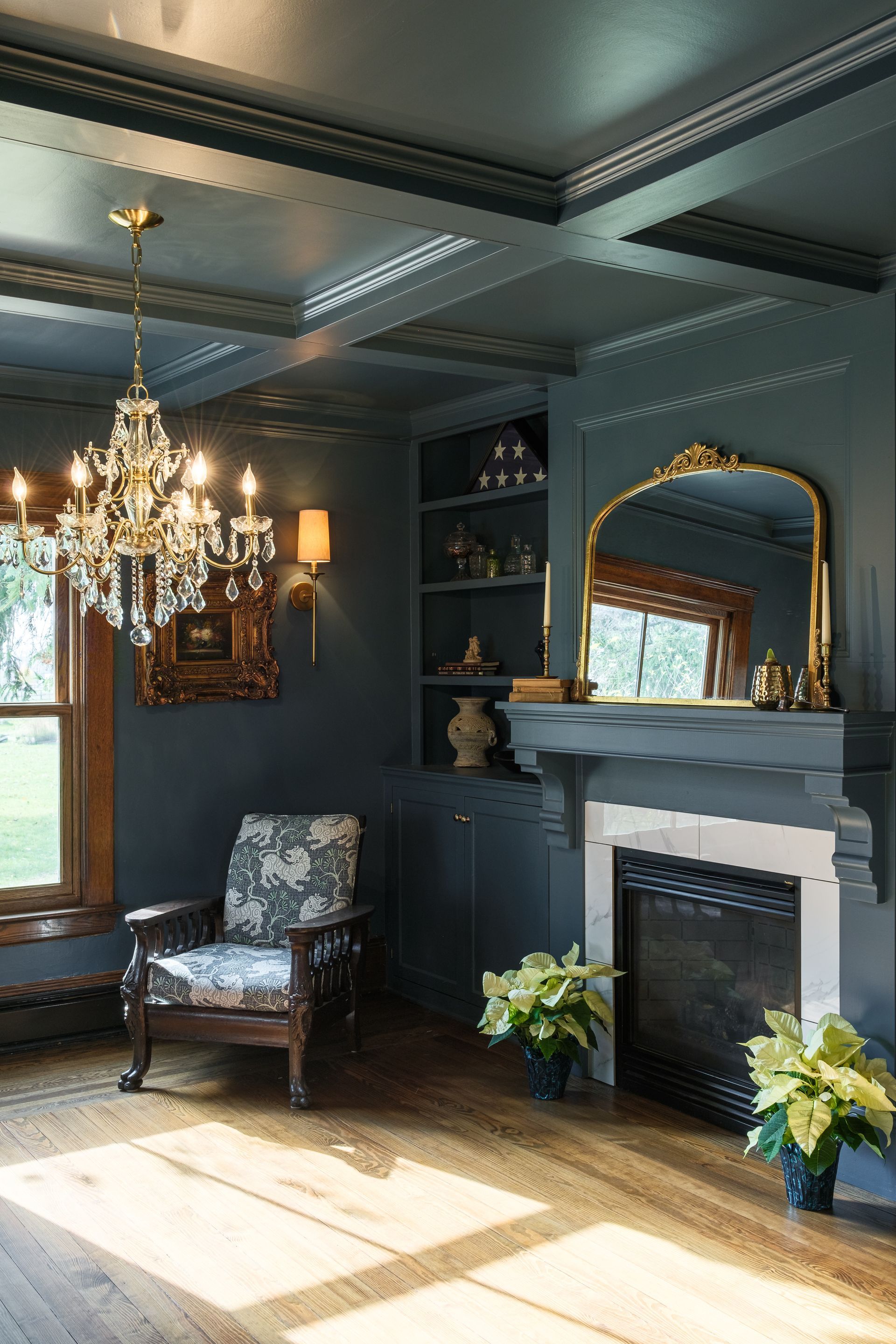 A living room with a fireplace , chair , mirror and chandelier.