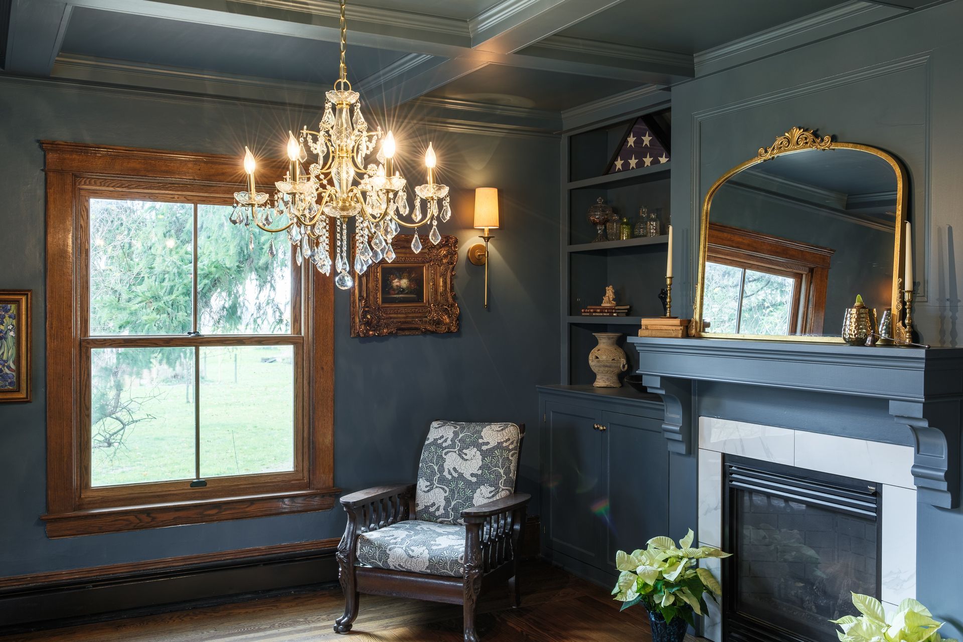 A living room with a fireplace , chair , mirror and chandelier.