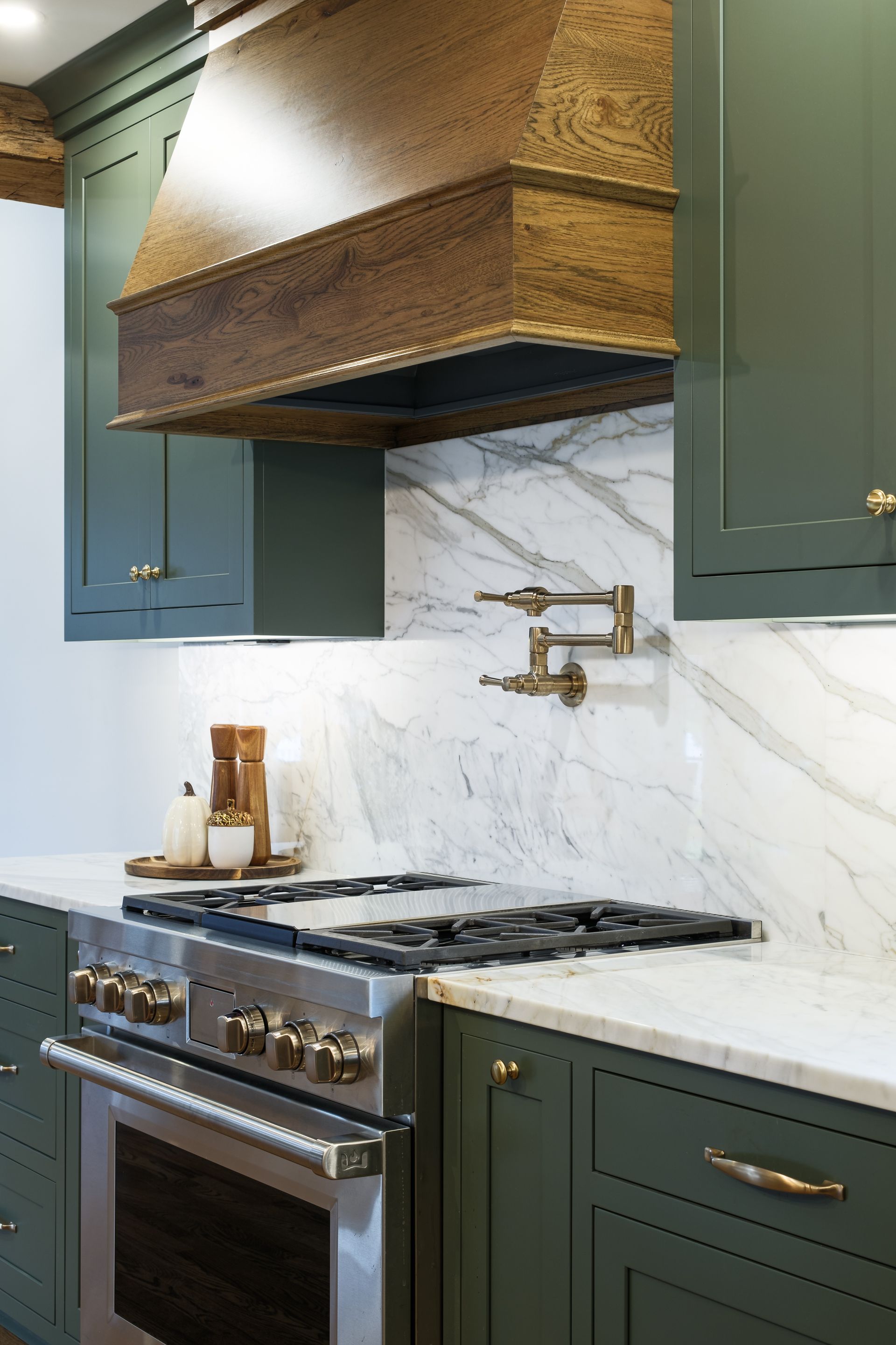 Green kitchen with marble backsplash, stainless steel oven, and wooden range hood.
