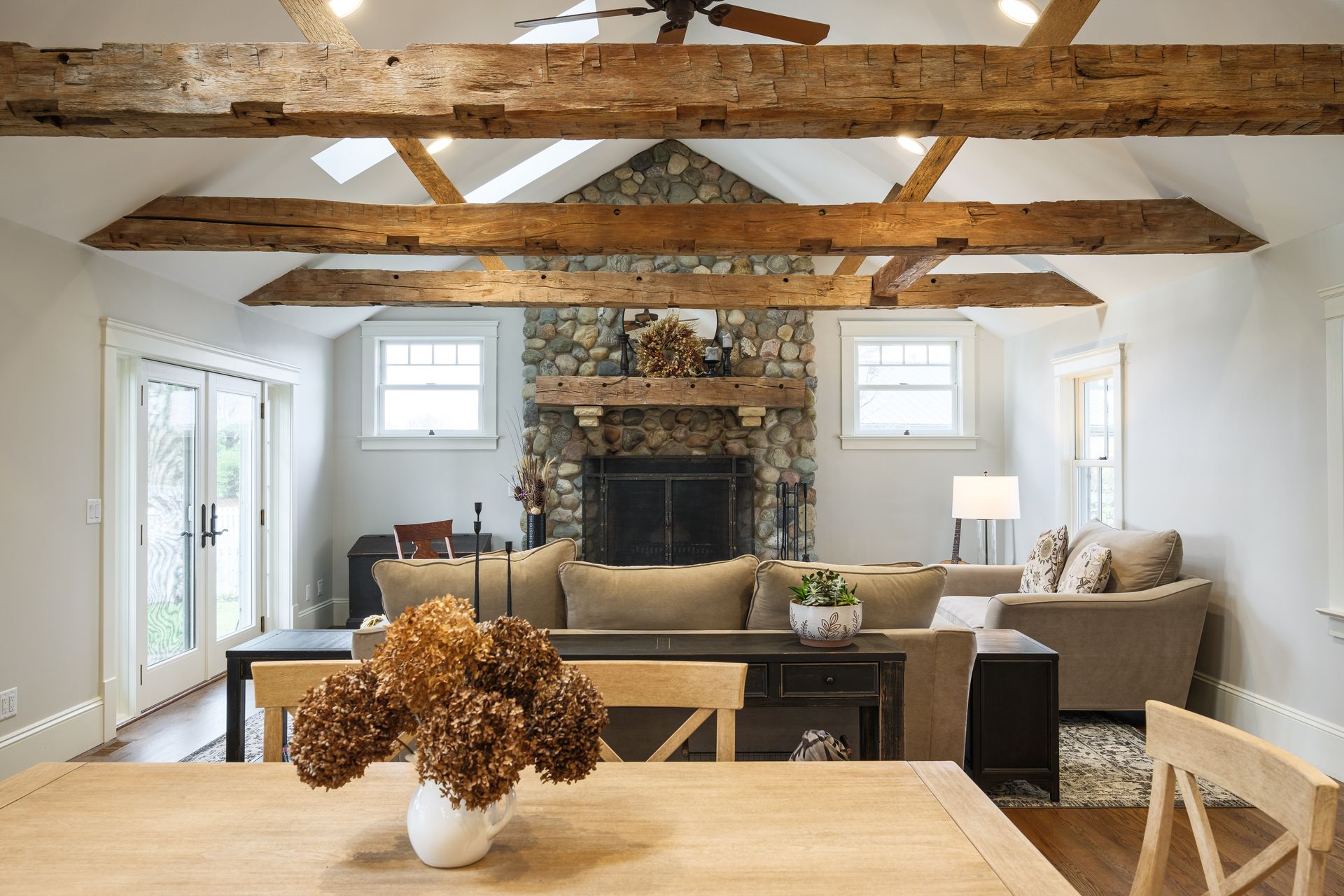 Living room with exposed wood beams, stone fireplace, light gray walls, and natural light.