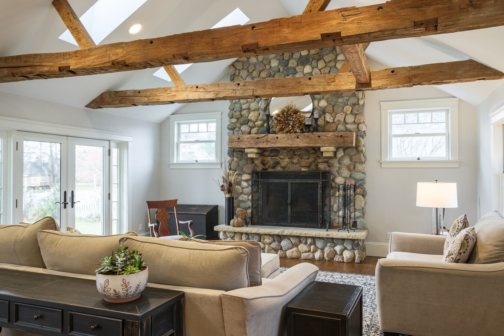 Living room with stone fireplace, wood beams, and neutral-toned furniture.