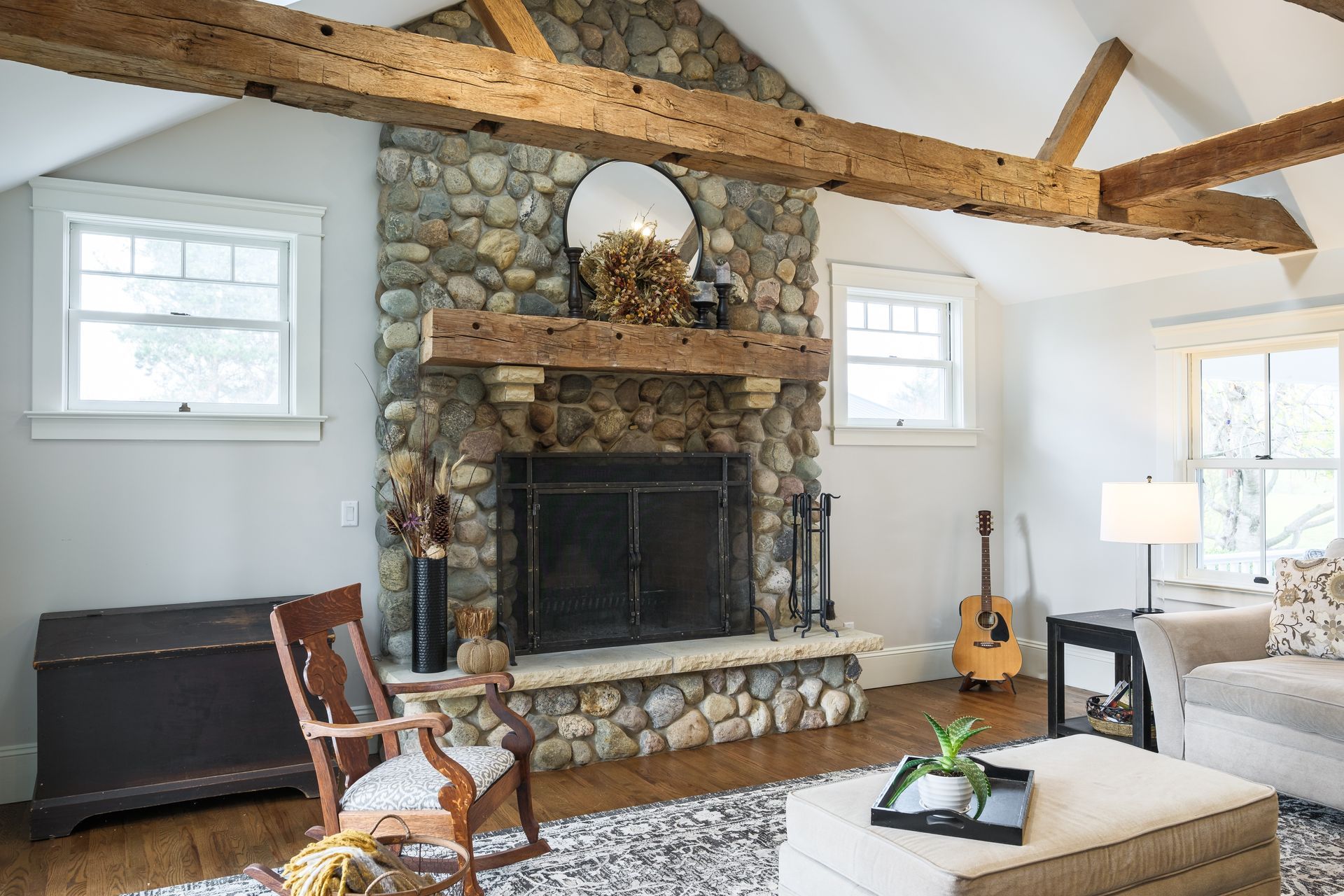 A living room with a fireplace , chairs , ottoman and guitar.