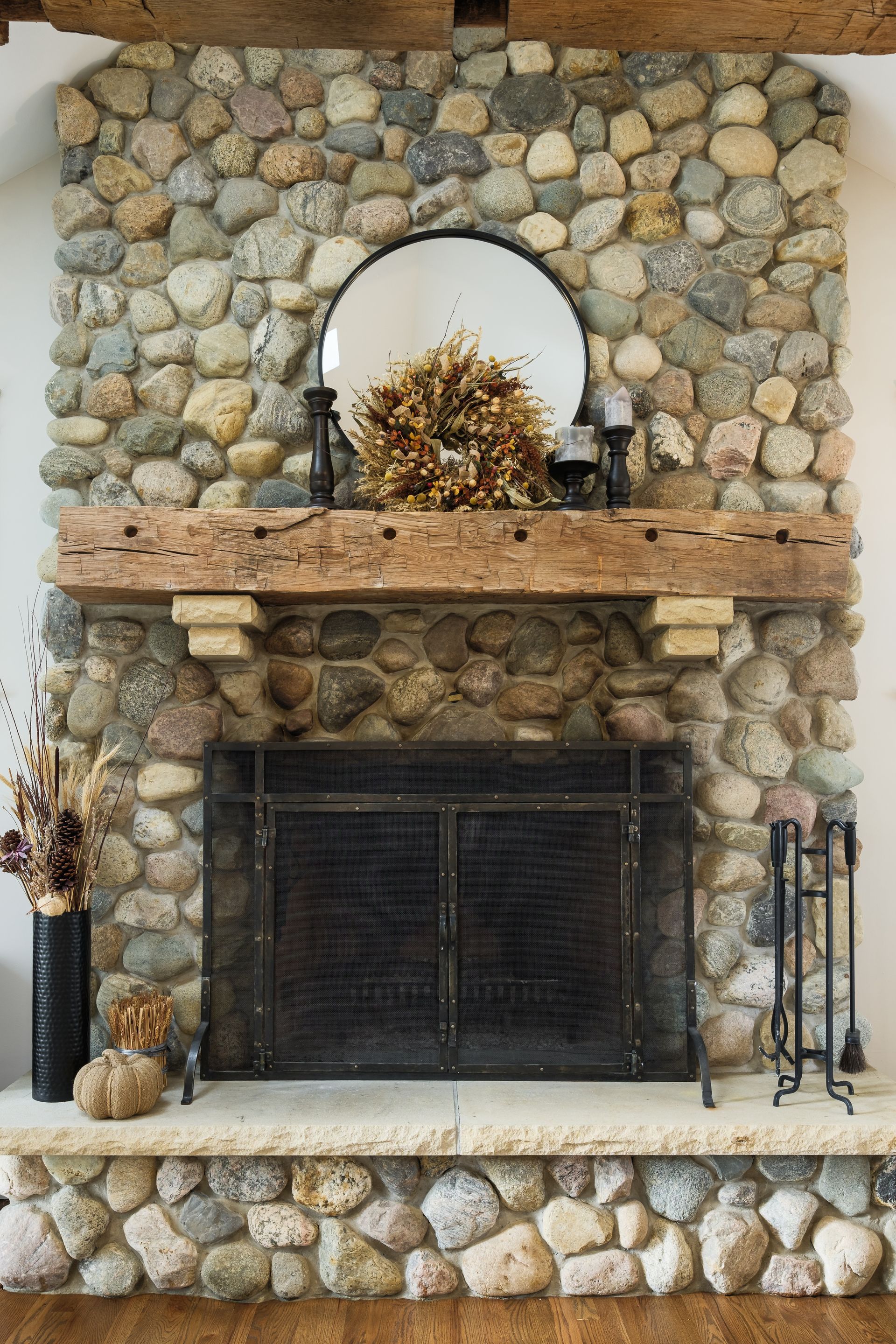 Stone fireplace with rustic wooden mantle, metal fire screen, and mirror.