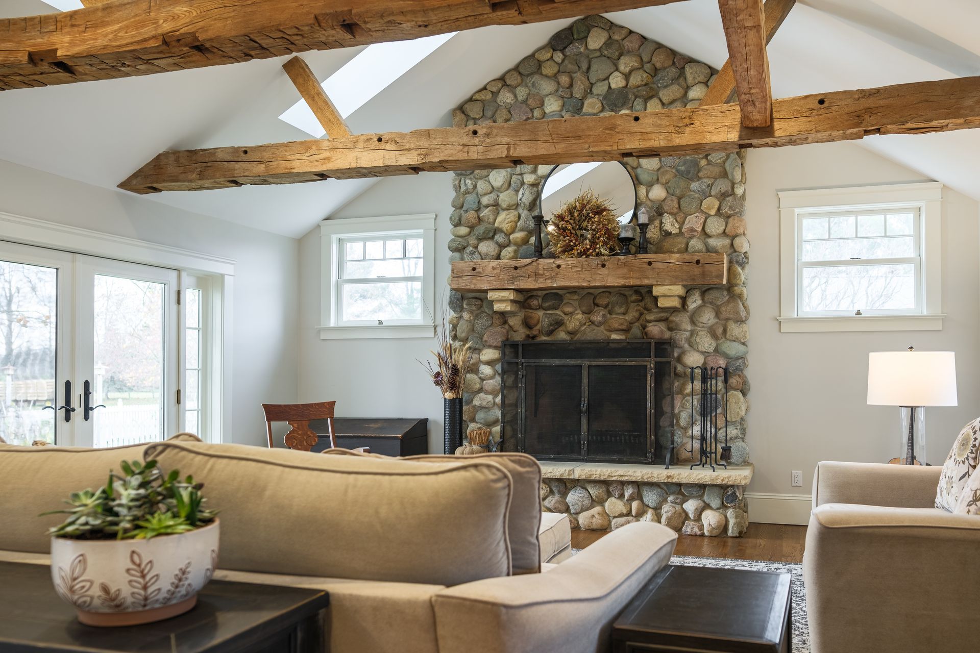 Living room with stone fireplace, wood beams, and neutral-toned furniture.