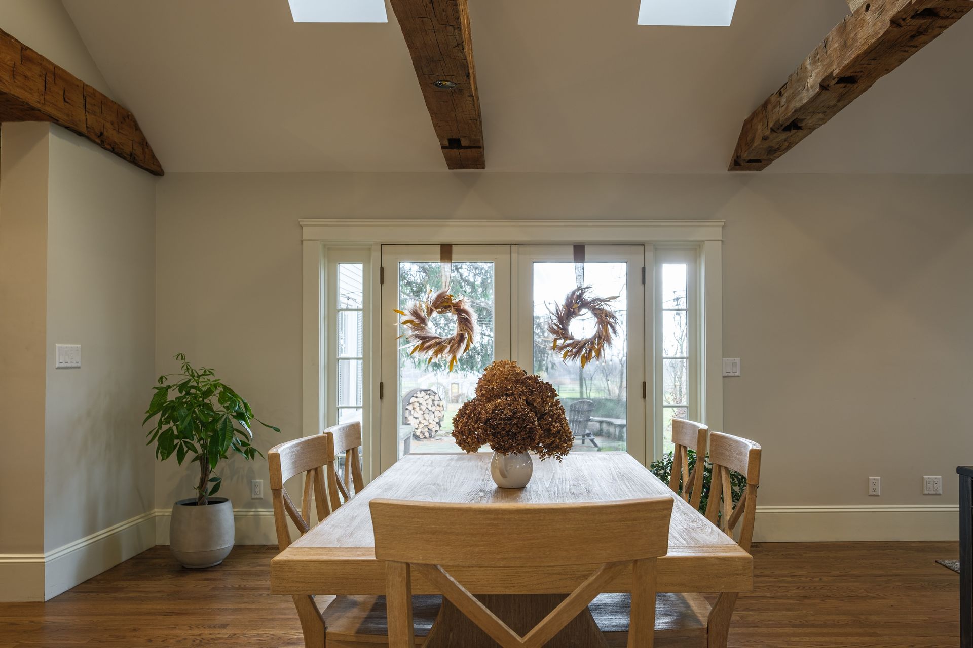 Dining room with a wooden table and chairs, French doors, and decorative wreaths.