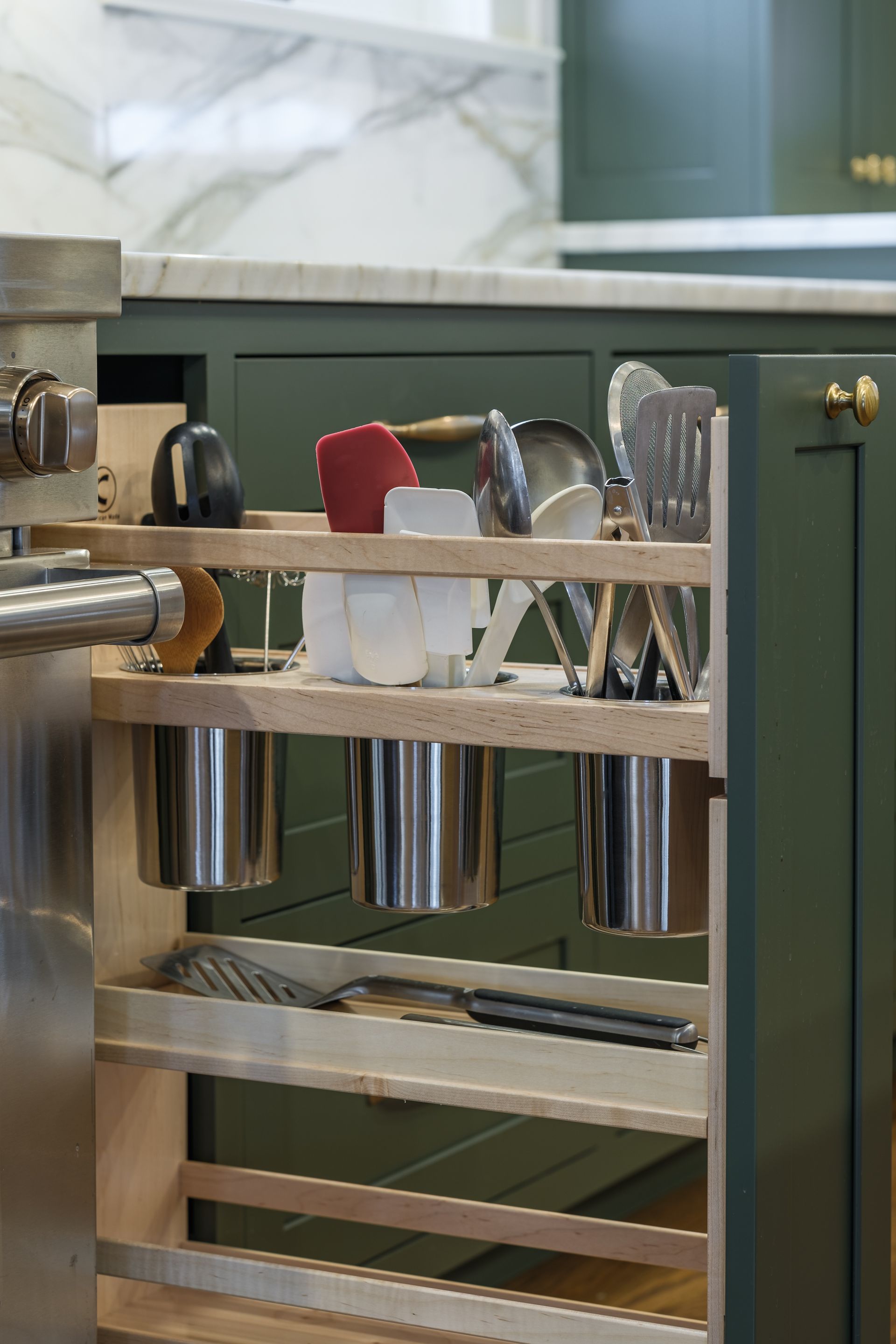 A kitchen with green cabinets and a pull out shelf with utensils on it.
