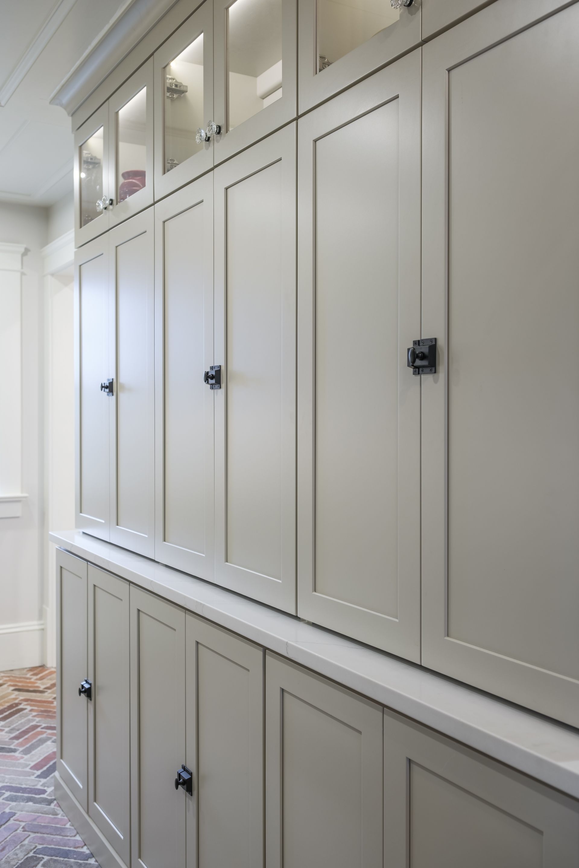 Tall, light gray storage cabinets with black hardware, some with glass doors, in a hallway setting.