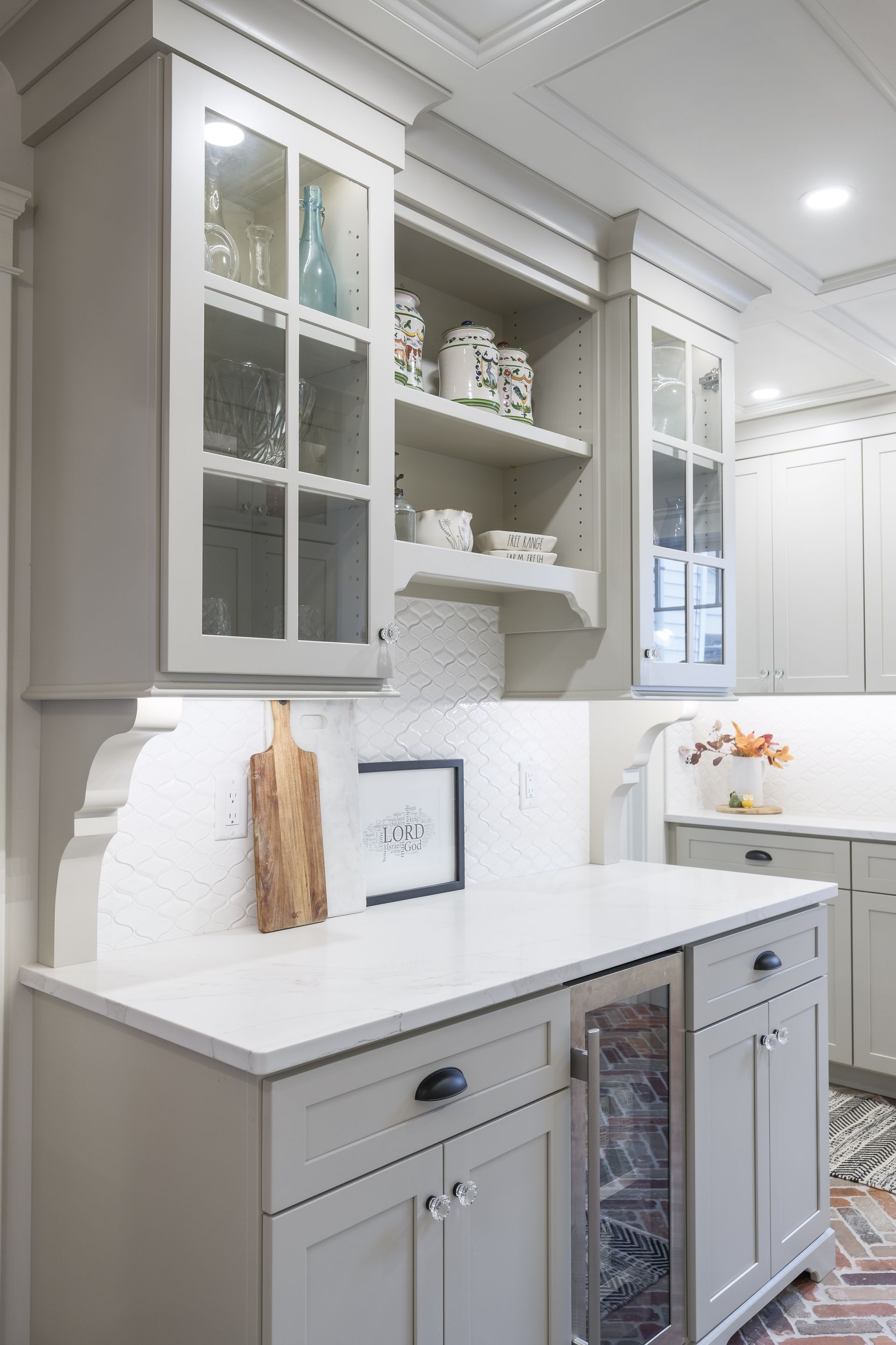 Gray kitchen cabinets with glass doors, white countertops, and decorative shelving.