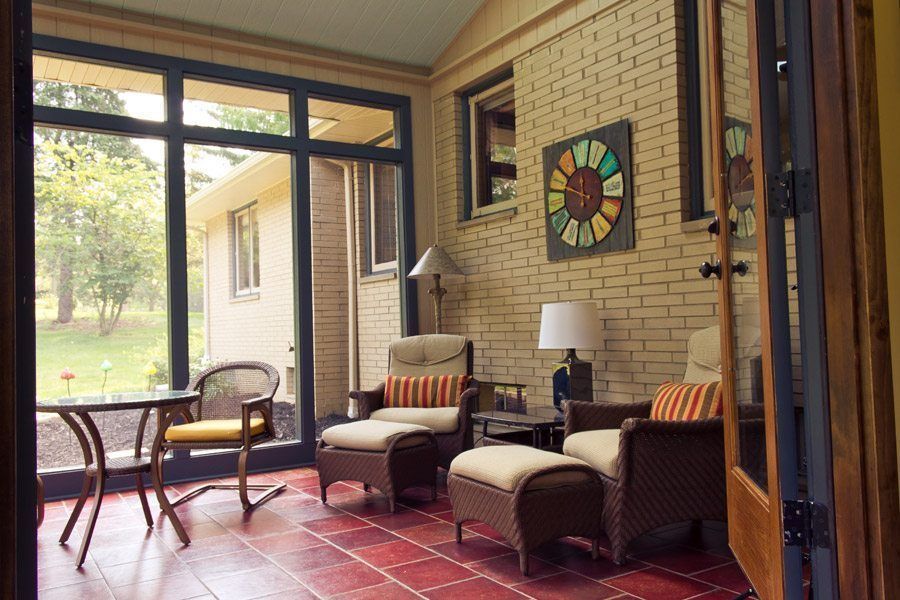 A sun room with chairs , a table and a clock on the wall.