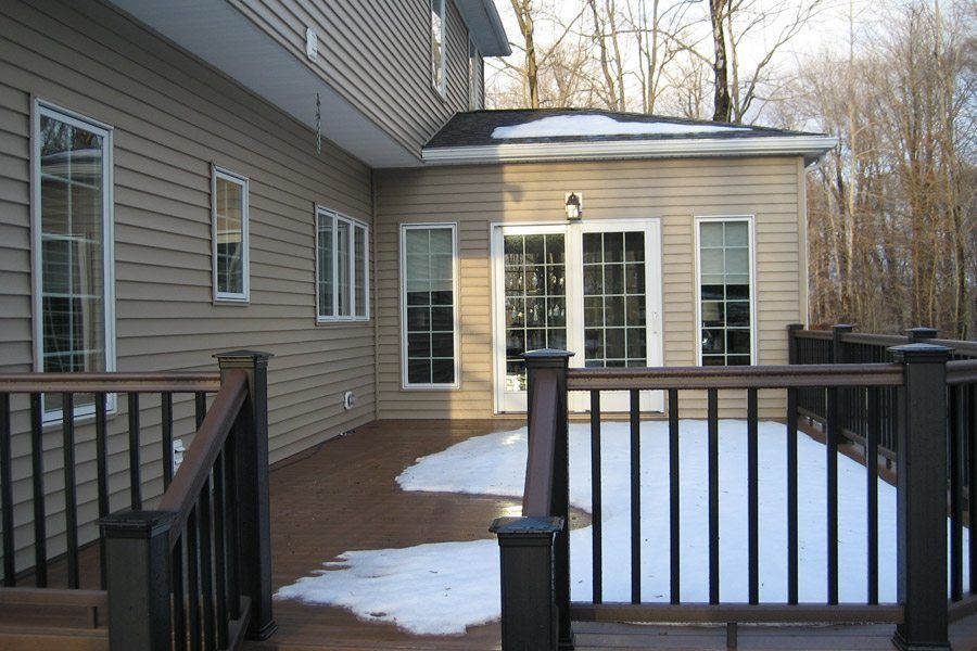 A deck with snow on it and a house in the background
