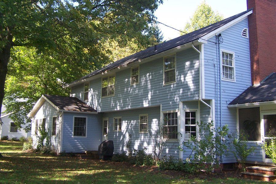 A blue house with a brick chimney is surrounded by trees