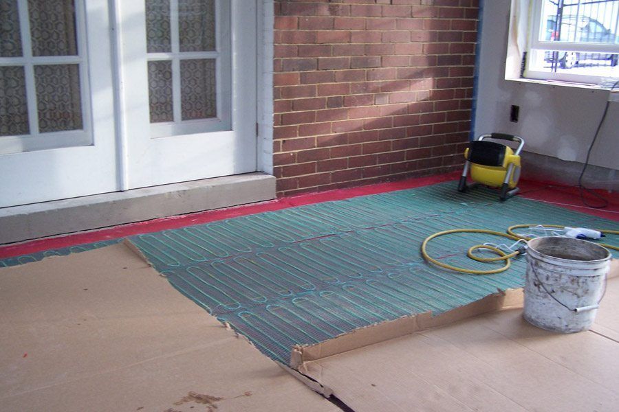 A bucket of paint sits on the floor in front of a brick wall