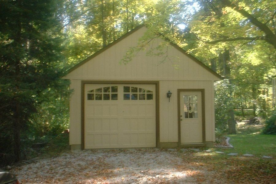 A white garage with a brown trim is surrounded by trees