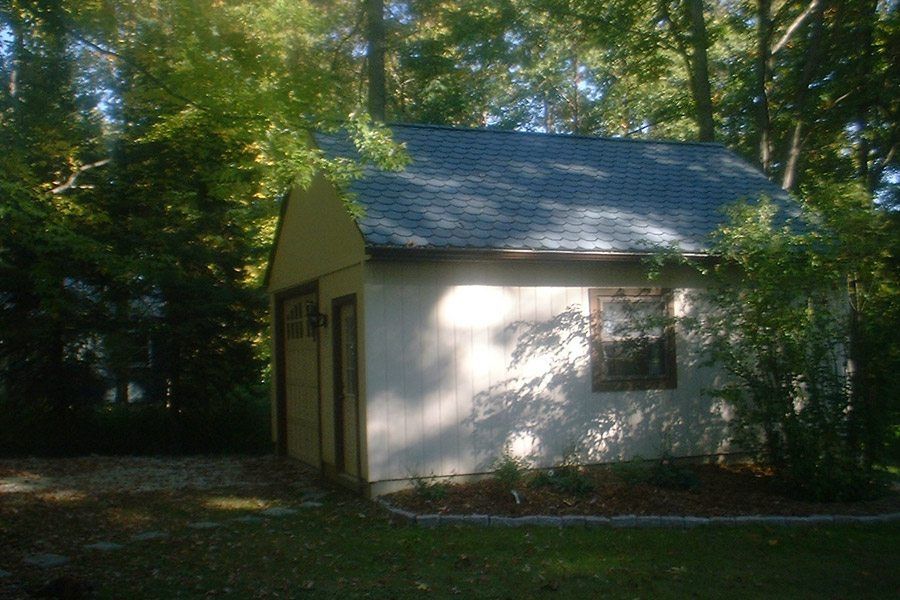 A white garage with a blue roof is surrounded by trees