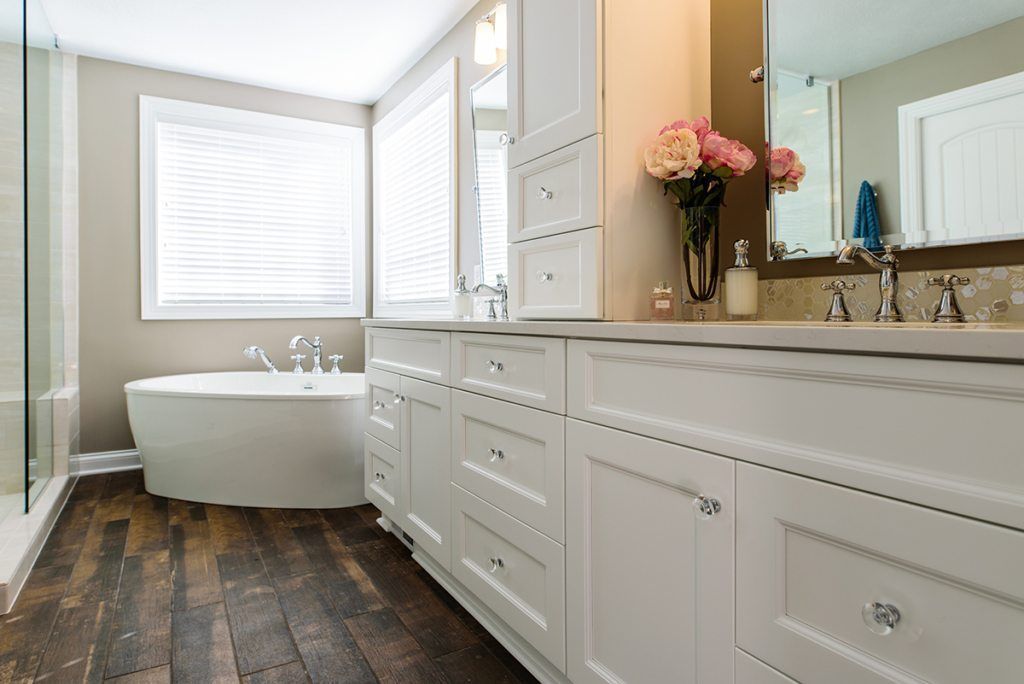 A bathroom with two sinks , a tub , and a mirror.