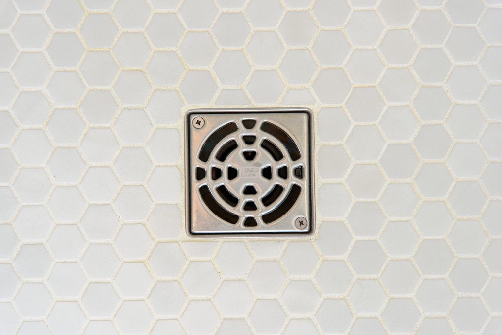 A close up of a shower drain on a white tile floor.