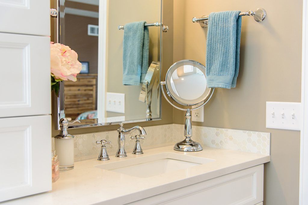 A bathroom with a sink , mirror , and towels hanging on the wall.