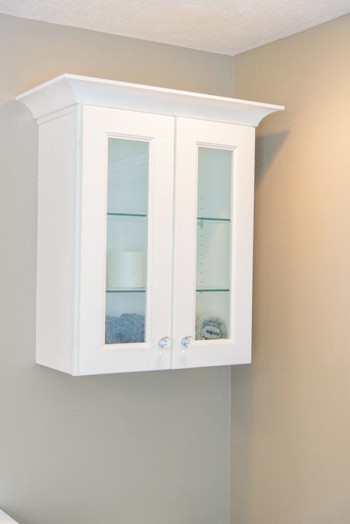 A white cabinet with glass doors is hanging on a wall.