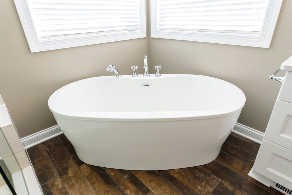 A white bathtub is sitting in the corner of a bathroom next to a window.