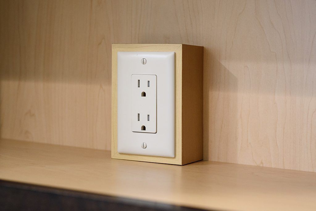 A white electrical outlet is sitting on a wooden shelf.